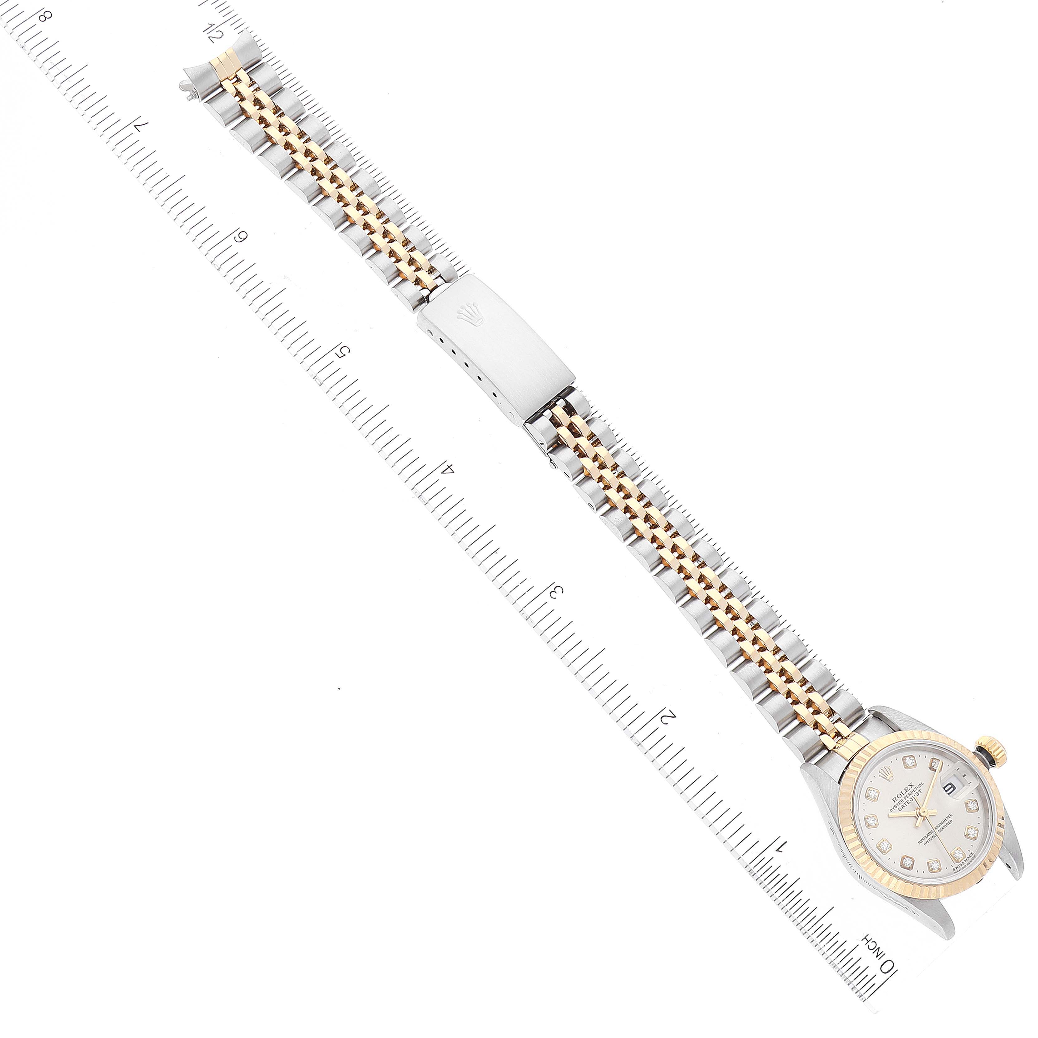 The image shows a Rolex Datejust 79173 Women
s Steel and Gold (two tone) Silver Dial 79173 Women
s Steel and Gold (two tone) Silver Dial watch laid flat on a ruler, highlighting its entire band and face from an overhead angle.