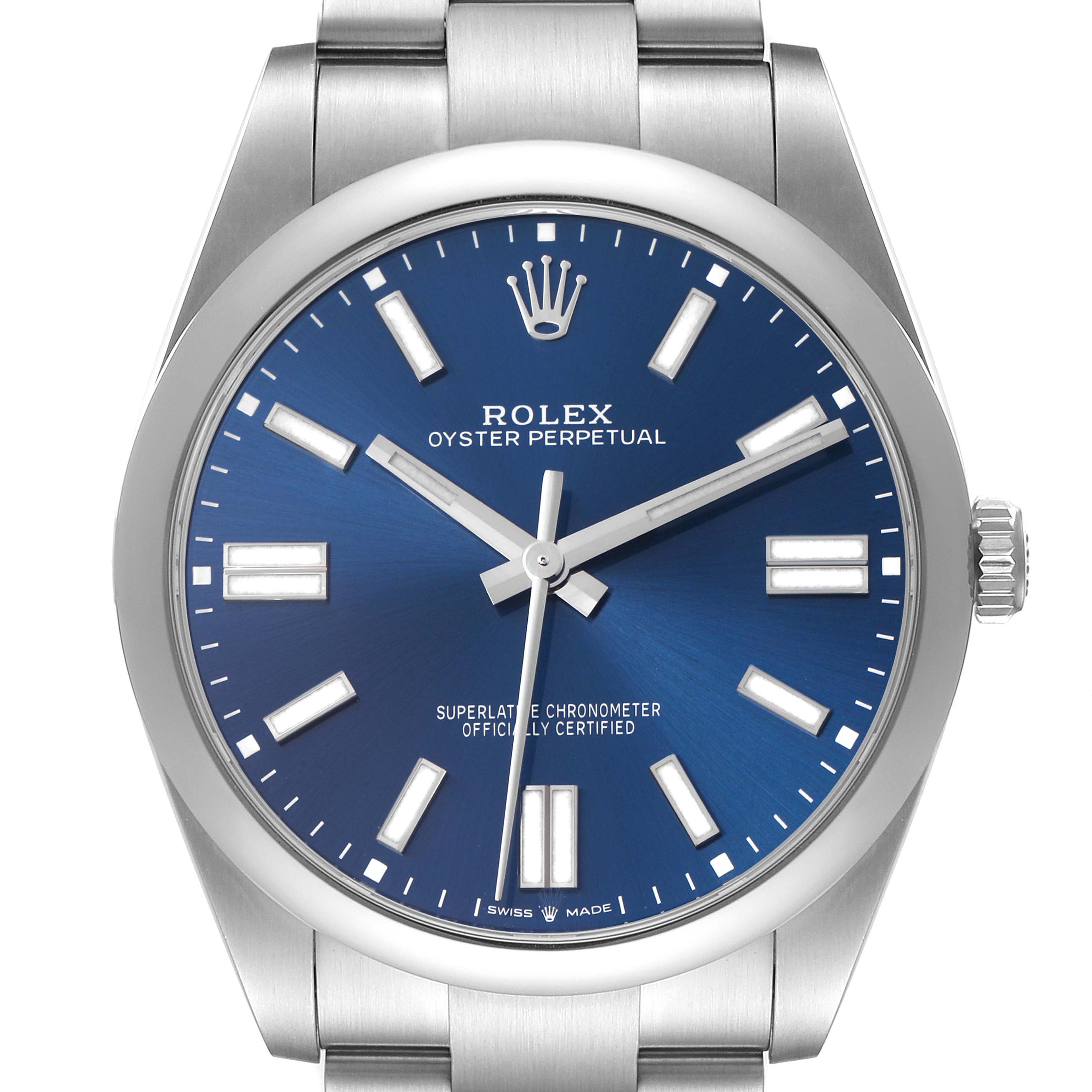 The Rolex Oyster Perpetual model 124300 is shown from a front angle, highlighting its blue dial, hour markers, hands, crown, and part of the metal bracelet.