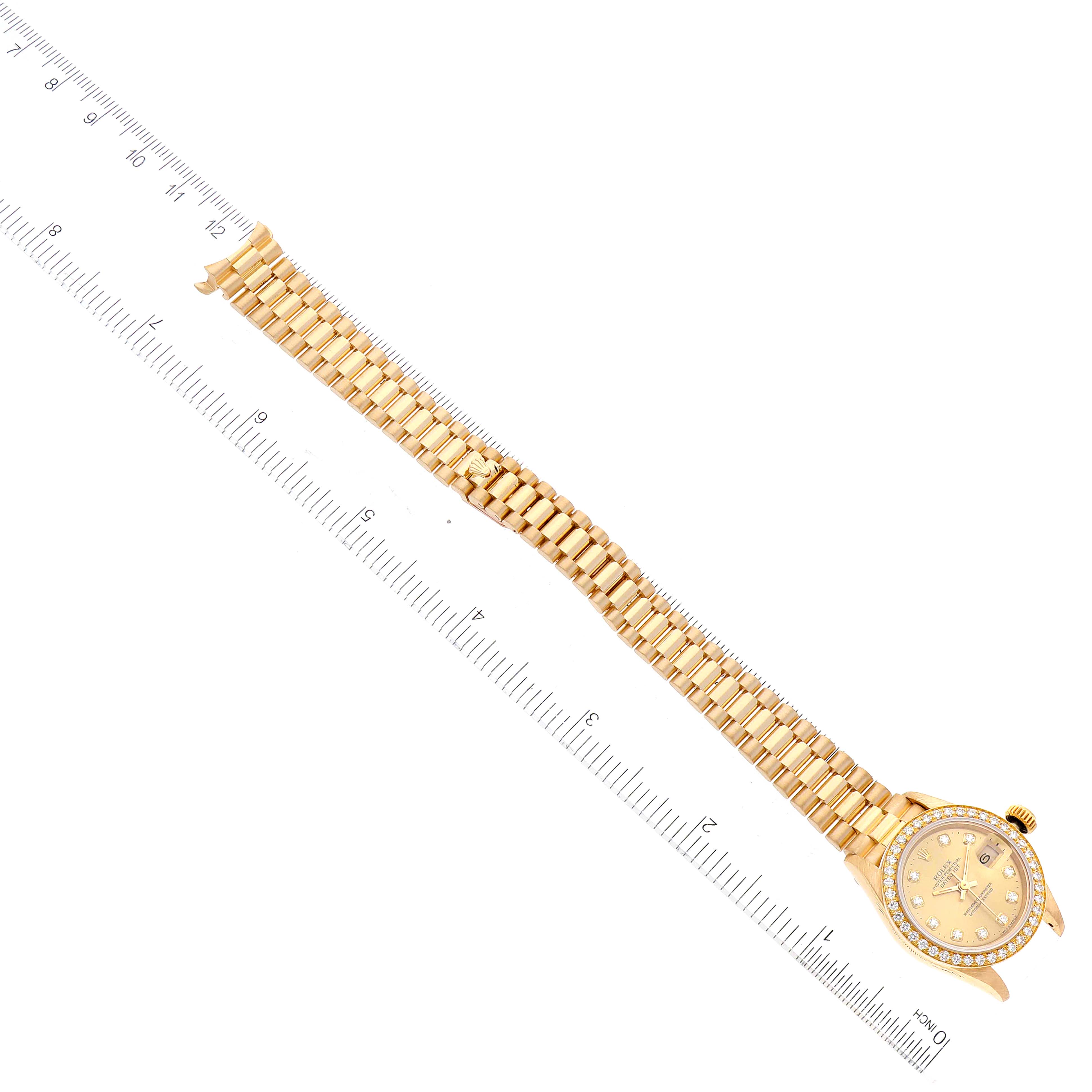 The image shows a Rolex President 69138 Women
s Yellow Gold Champagne Dial 69138 Women
s Yellow Gold Champagne Dial watch laid flat with its golden bracelet and face next to a ruler.