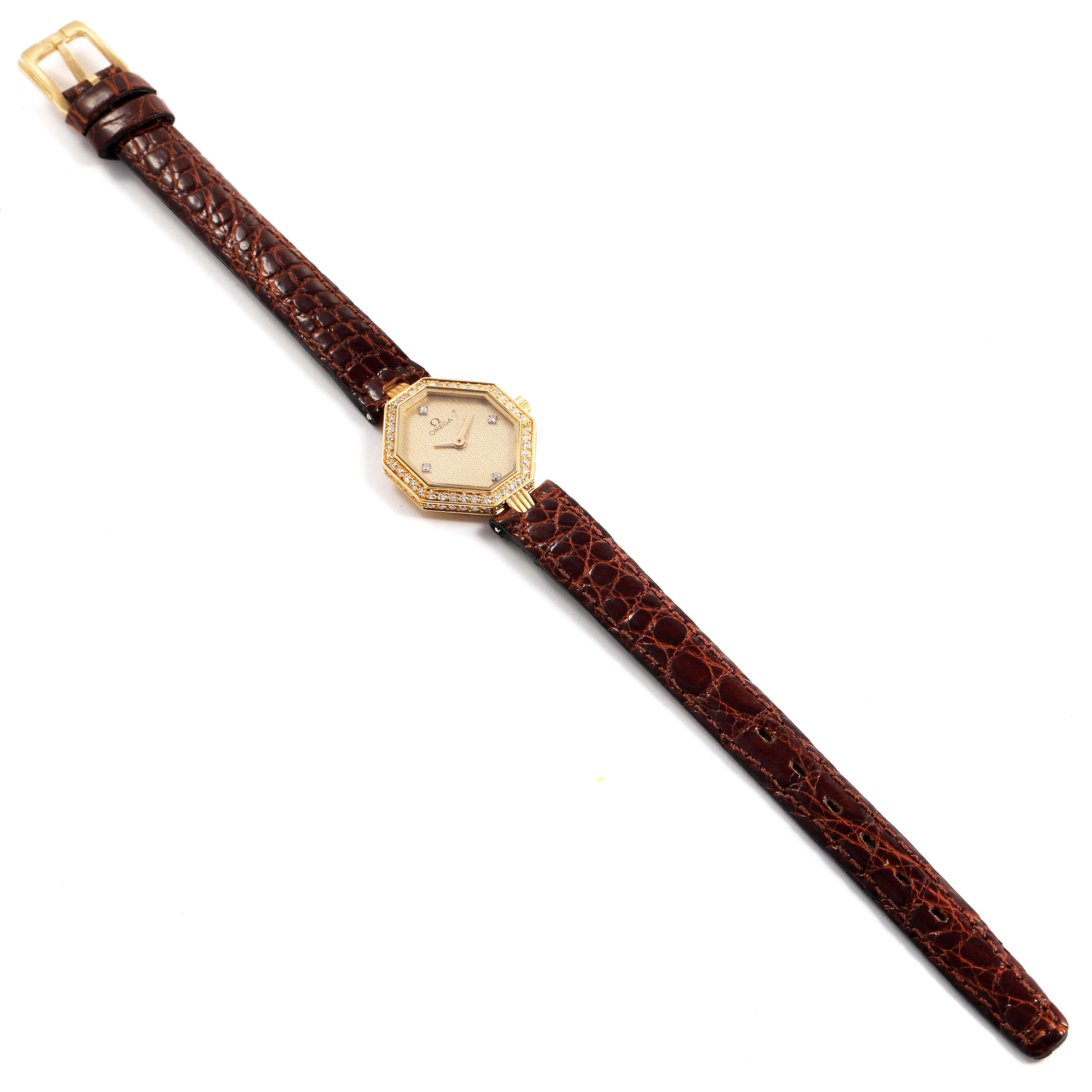 The Omega 1450 Women's Yellow Gold Champagne Dial 1450 Women's Yellow Gold Champagne Dial DeVille Mini Yellow Gold Diamond Cocktail Ladies Watch 1450 is shown from a top-down angle, displaying its brown leather strap and diamond-set octagonal face.