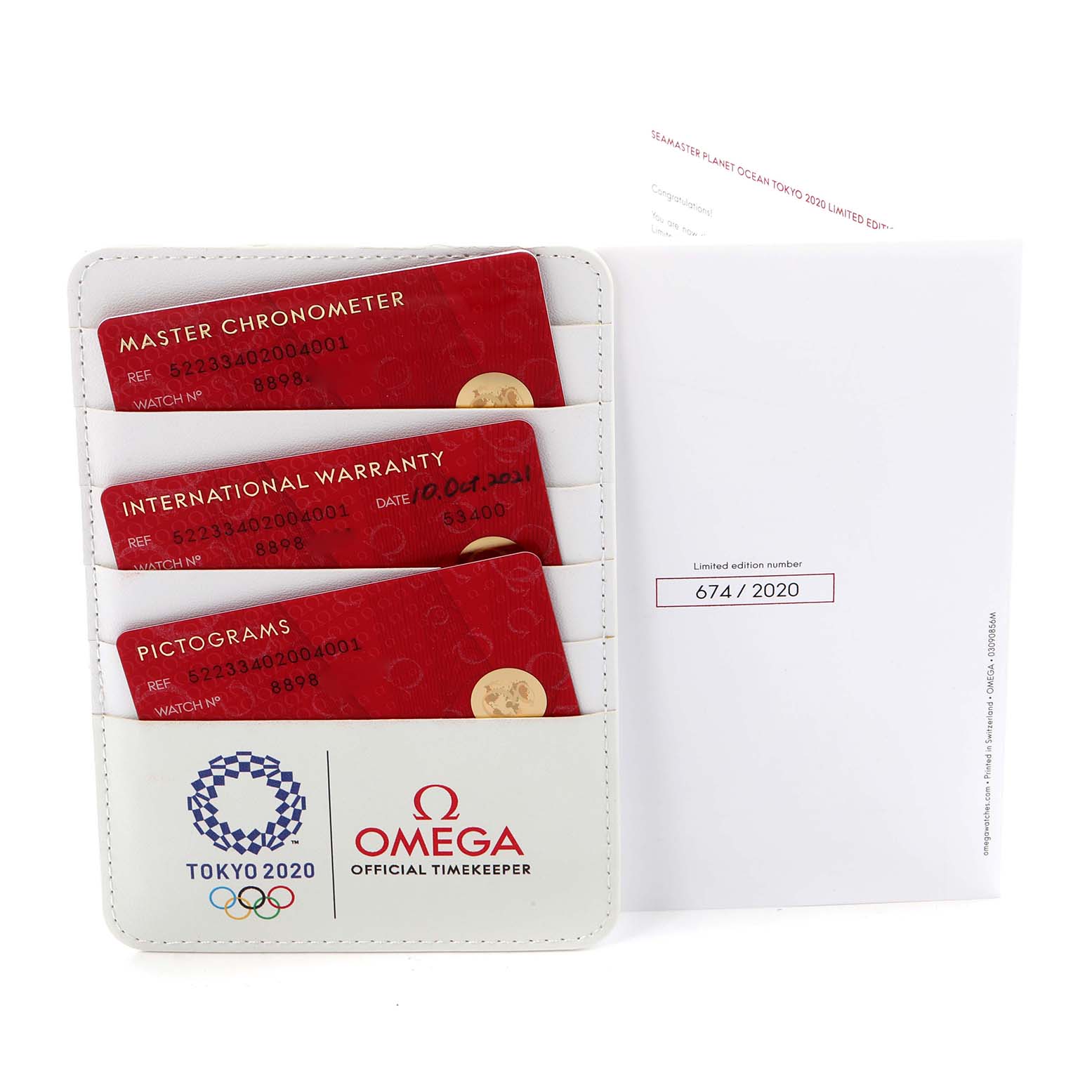 The image shows the warranty and pictogram cards for the Omega Planet Ocean model 522.33.40.20.04.001, displayed in a holder, with Tokyo 2020 branding.