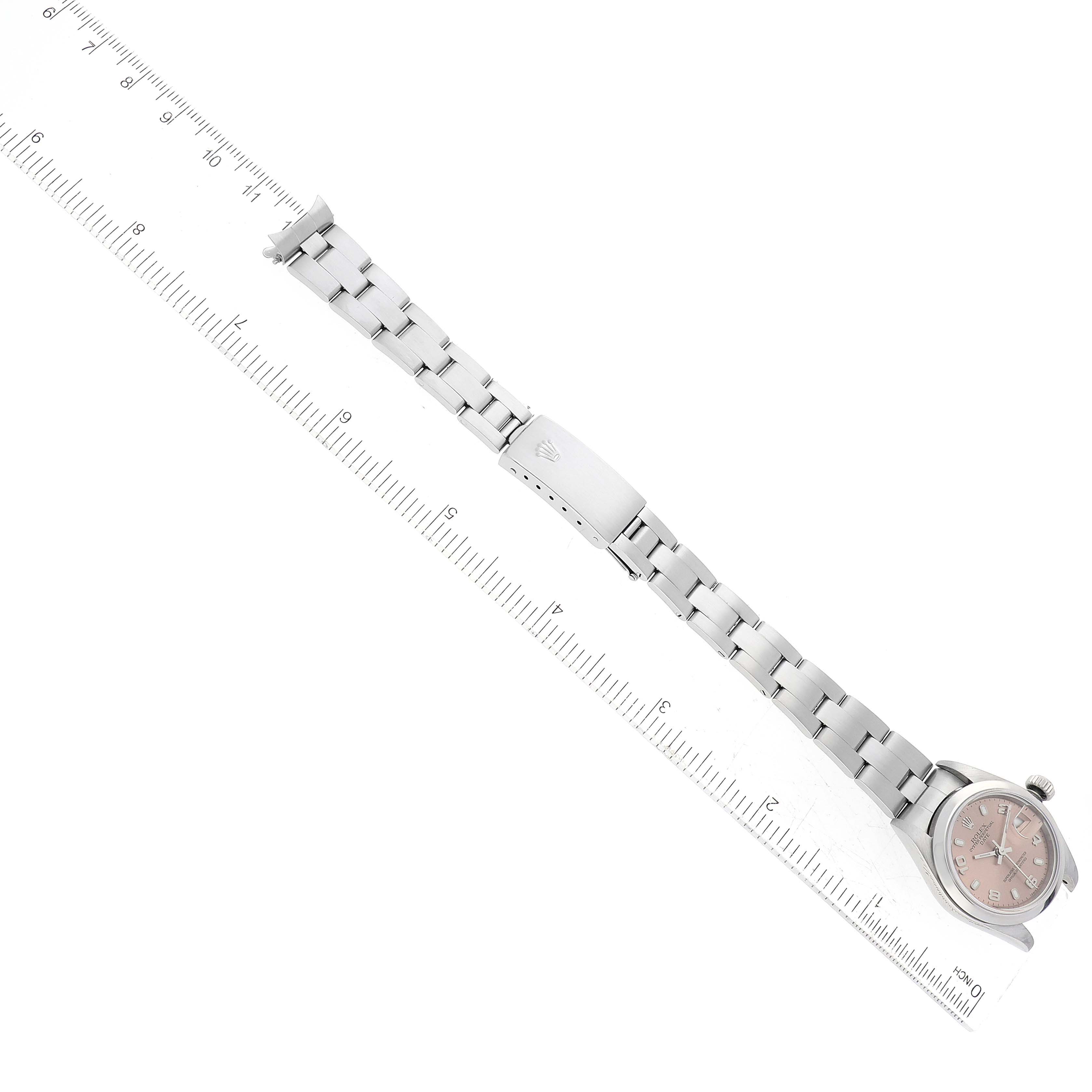 The Rolex Date 79160 Women's Stainless Steel Pink Dial 79160 Women's Stainless Steel Pink Dial model watch is shown diagonally with its face, bracelet, and clasp visible alongside a ruler for scale.