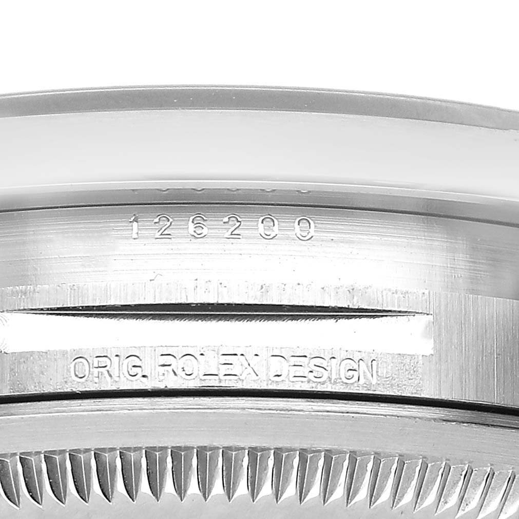 The image shows a close-up of the edge of a Rolex Datejust 126200 Men's Stainless Steel Blue Dial watch case, displaying the model number and "ORIG. ROLEX DESIGN" engraving.