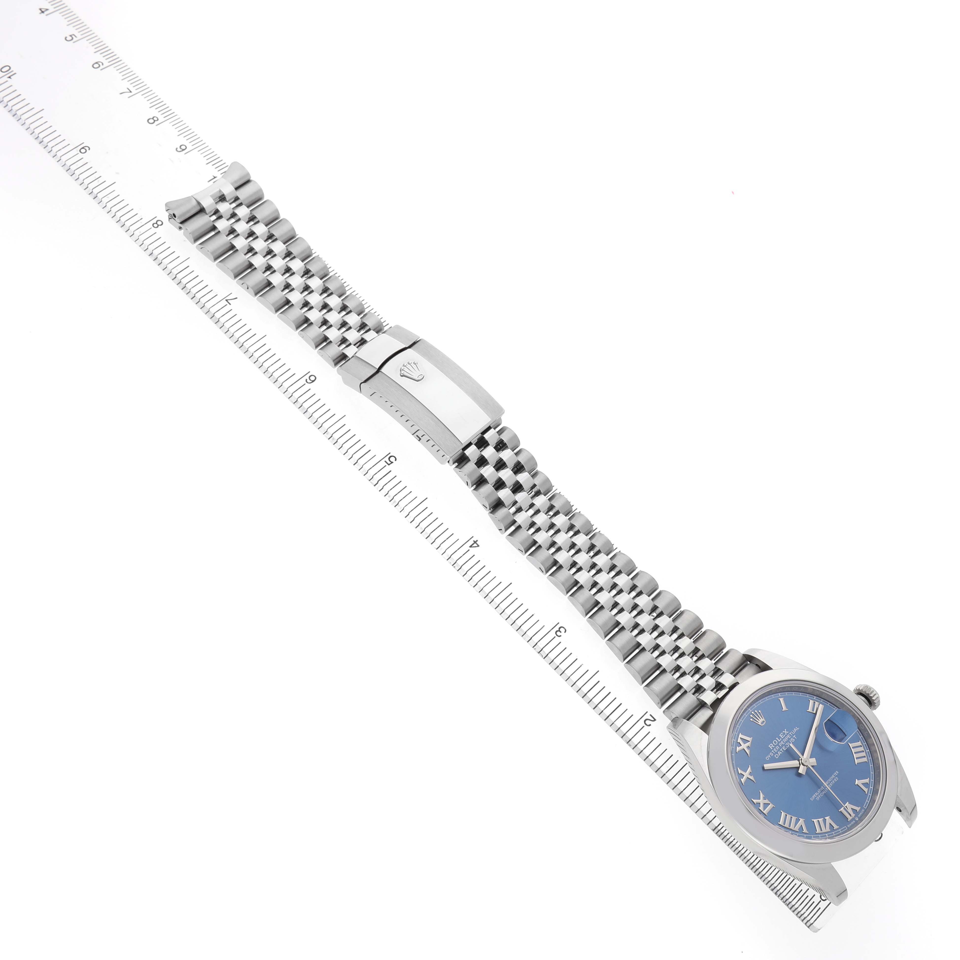 The Rolex Datejust 41 126300 Men's Stainless Steel Blue Dial watch is shown at a diagonal angle, highlighting the blue dial, bracelet, and clasp beside a ruler.