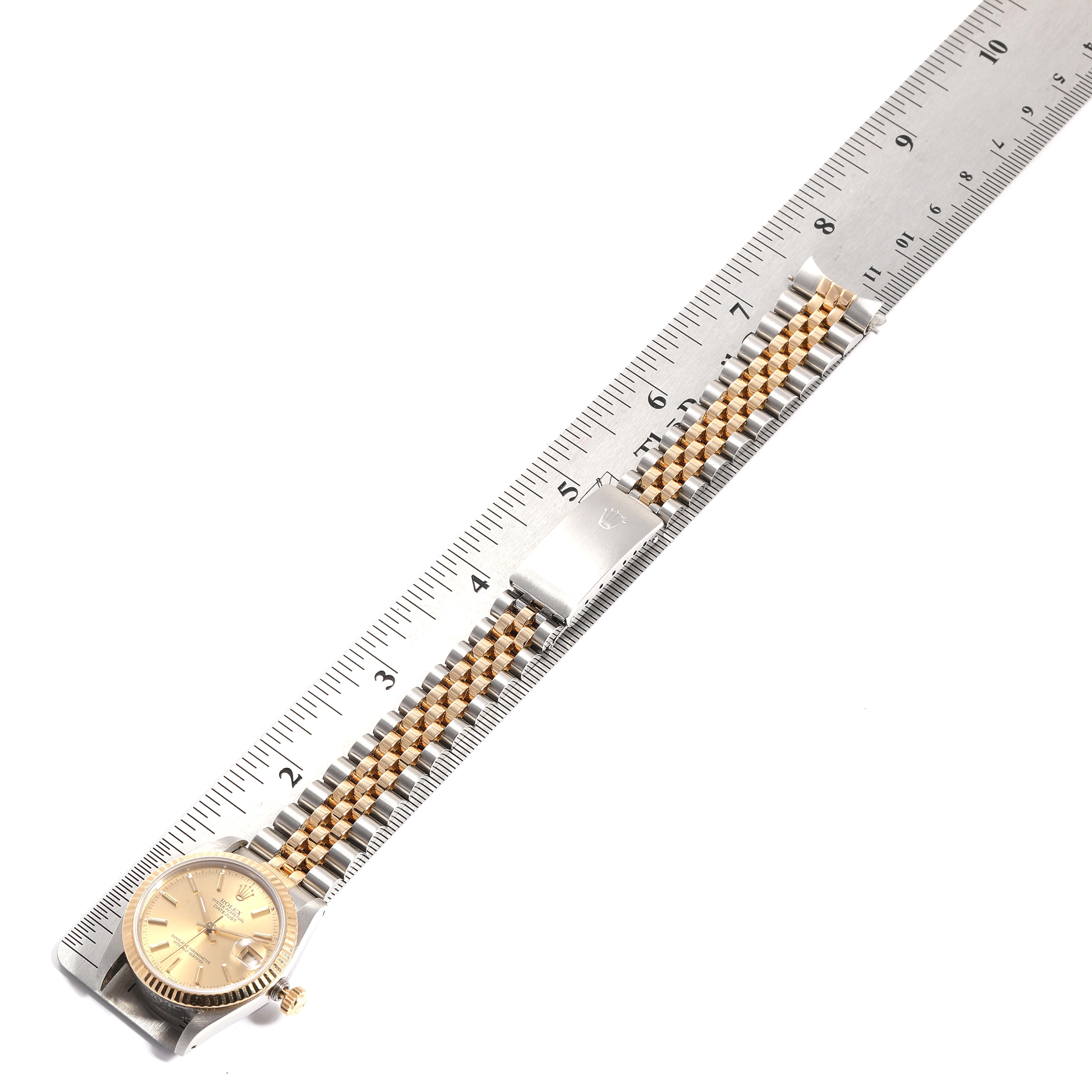 The image shows a Rolex Mid-Size 68273 Women
s Steel and Gold (two tone) Champagne Dial 68273 Women
s Steel and Gold (two tone) Champagne Dial watch, with the dial, crown, bracelet, and clasp displayed at an oblique angle next to a ruler.