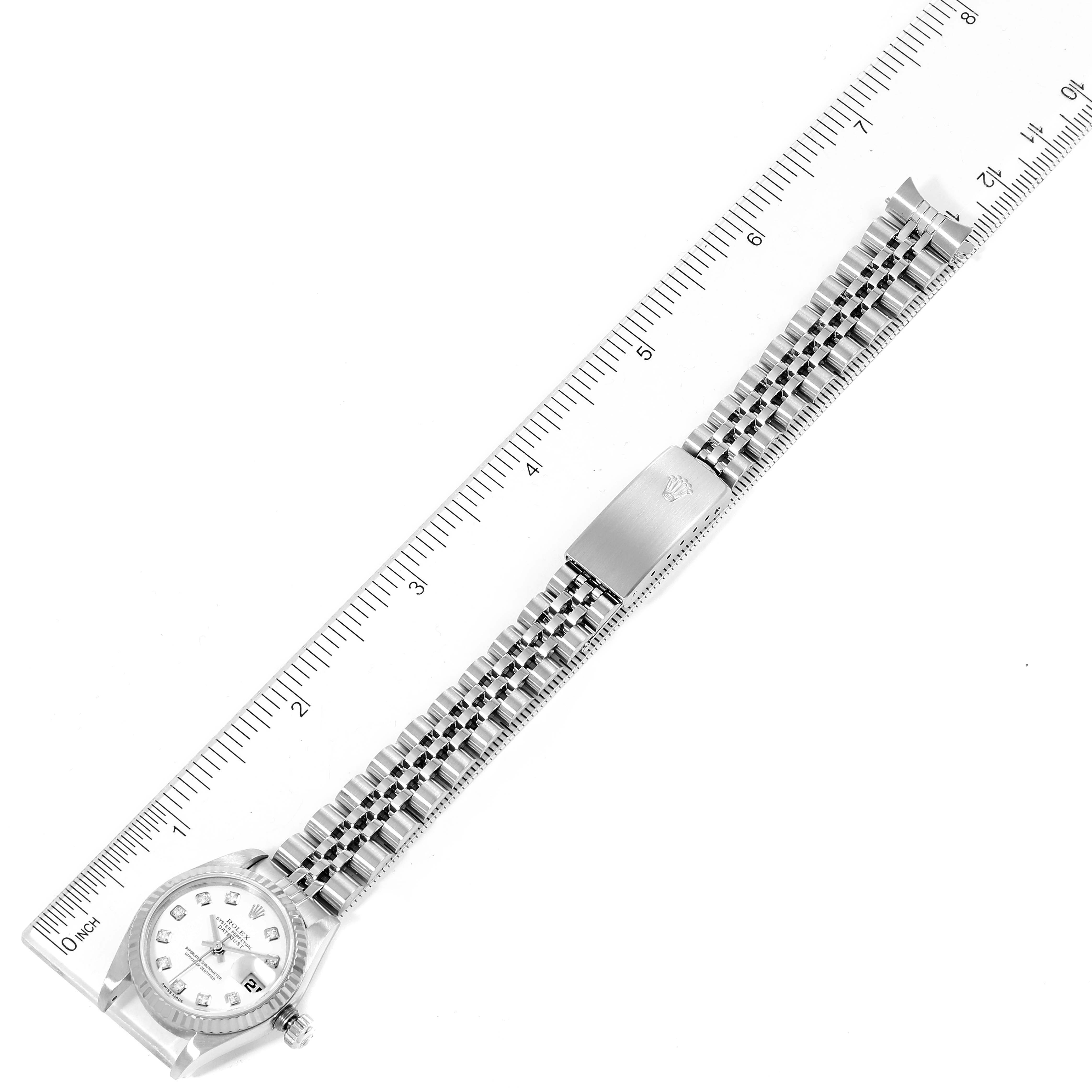 The image shows a flat, top-down view of a Rolex Datejust 79174 Women
s Stainless Steel White Dial 79174 Women
s Stainless Steel White Dial watch, displaying the full bracelet and the face beside a ruler.