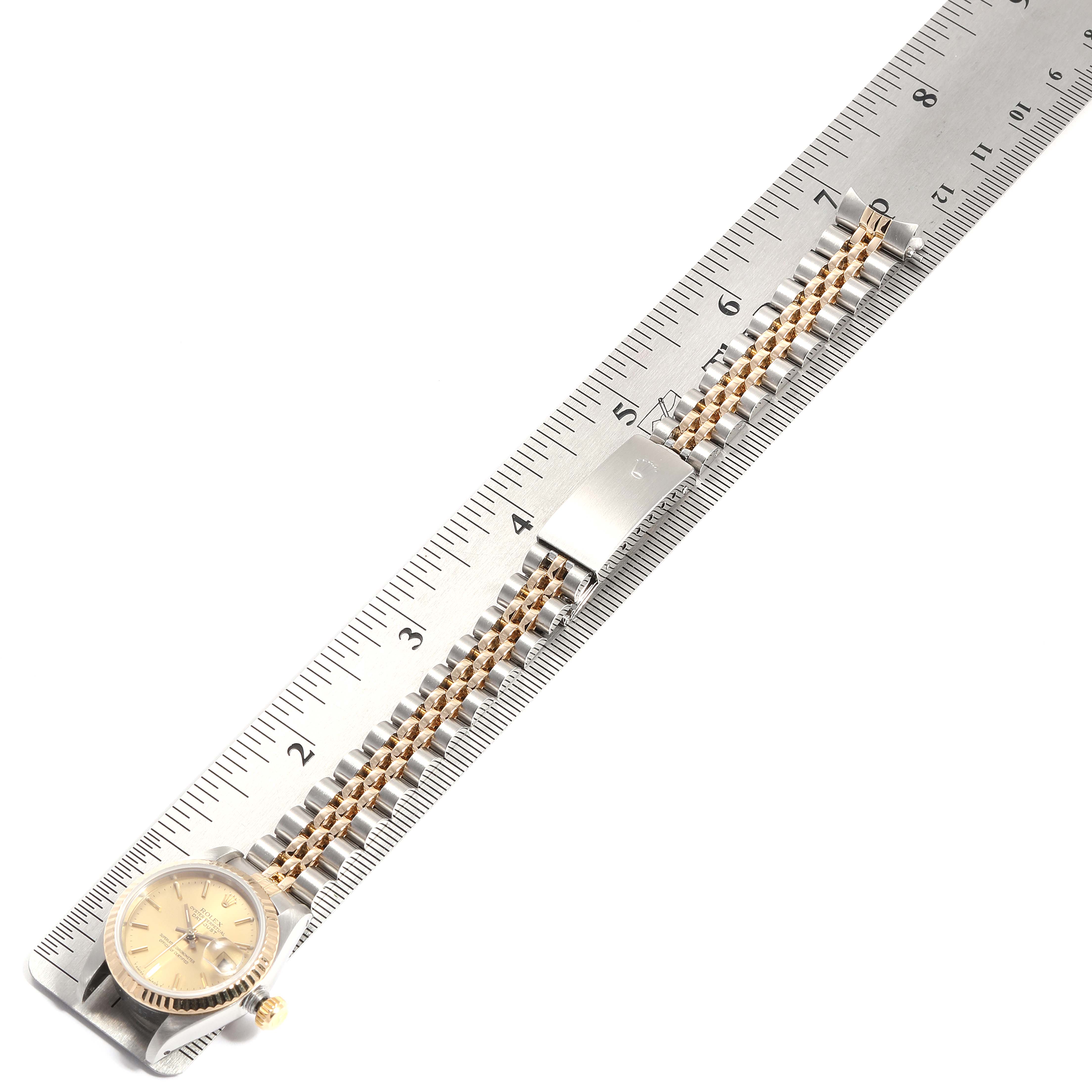 This image shows a Rolex Datejust 69173 Women
s Steel and Gold (two tone) Champagne Dial 69173 Women
s Steel and Gold (two tone) Champagne Dial watch placed diagonally against a ruler, featuring the watch face and bracelet links.