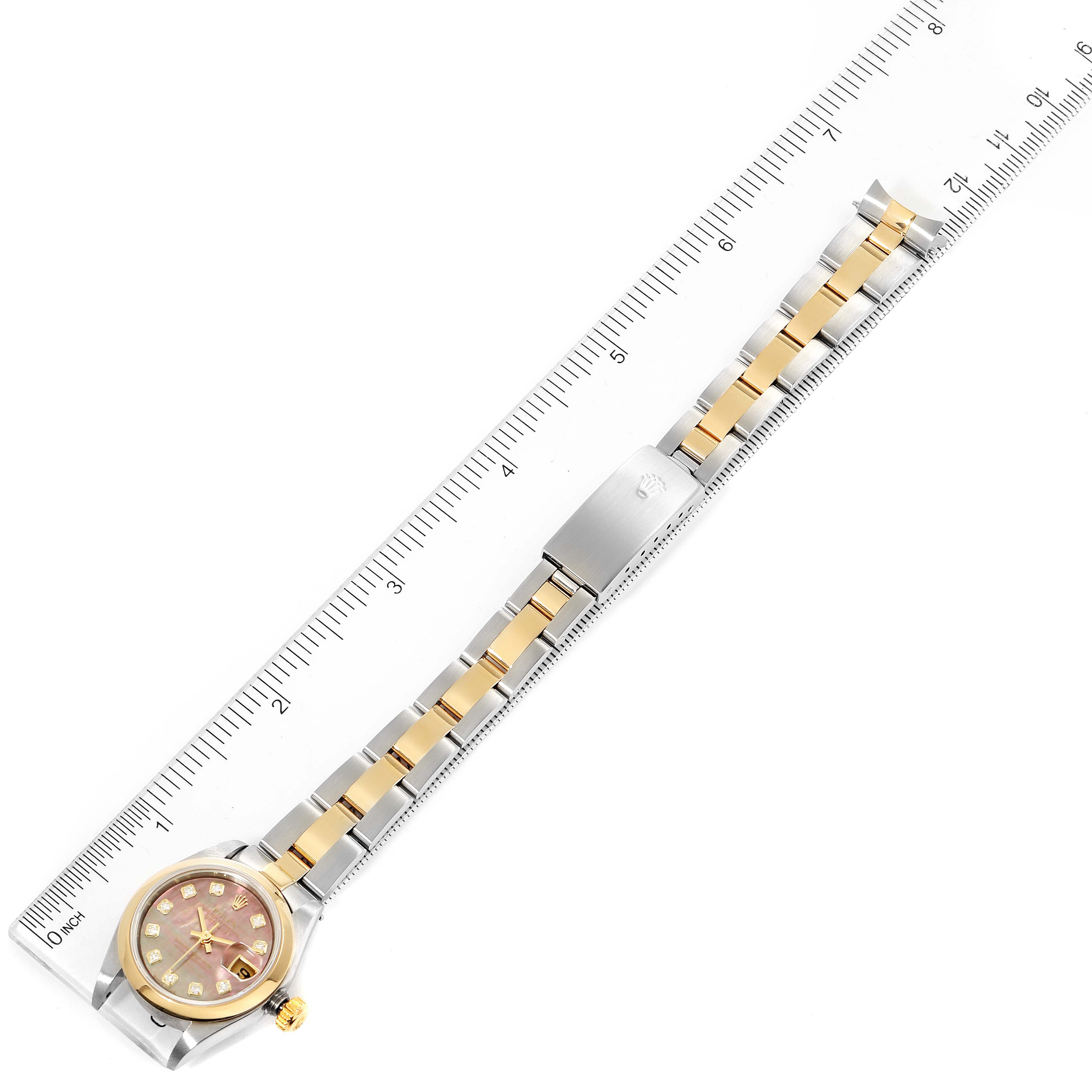 The image shows a Rolex Datejust 79163 Women
s Steel and Gold (two tone) Mother of Pearl Dial 79163 Women
s Steel and Gold (two tone) Mother of Pearl Dial watch from a top-down angle, fully displaying its strap, clasp, and face, alongside a ruler for scale.