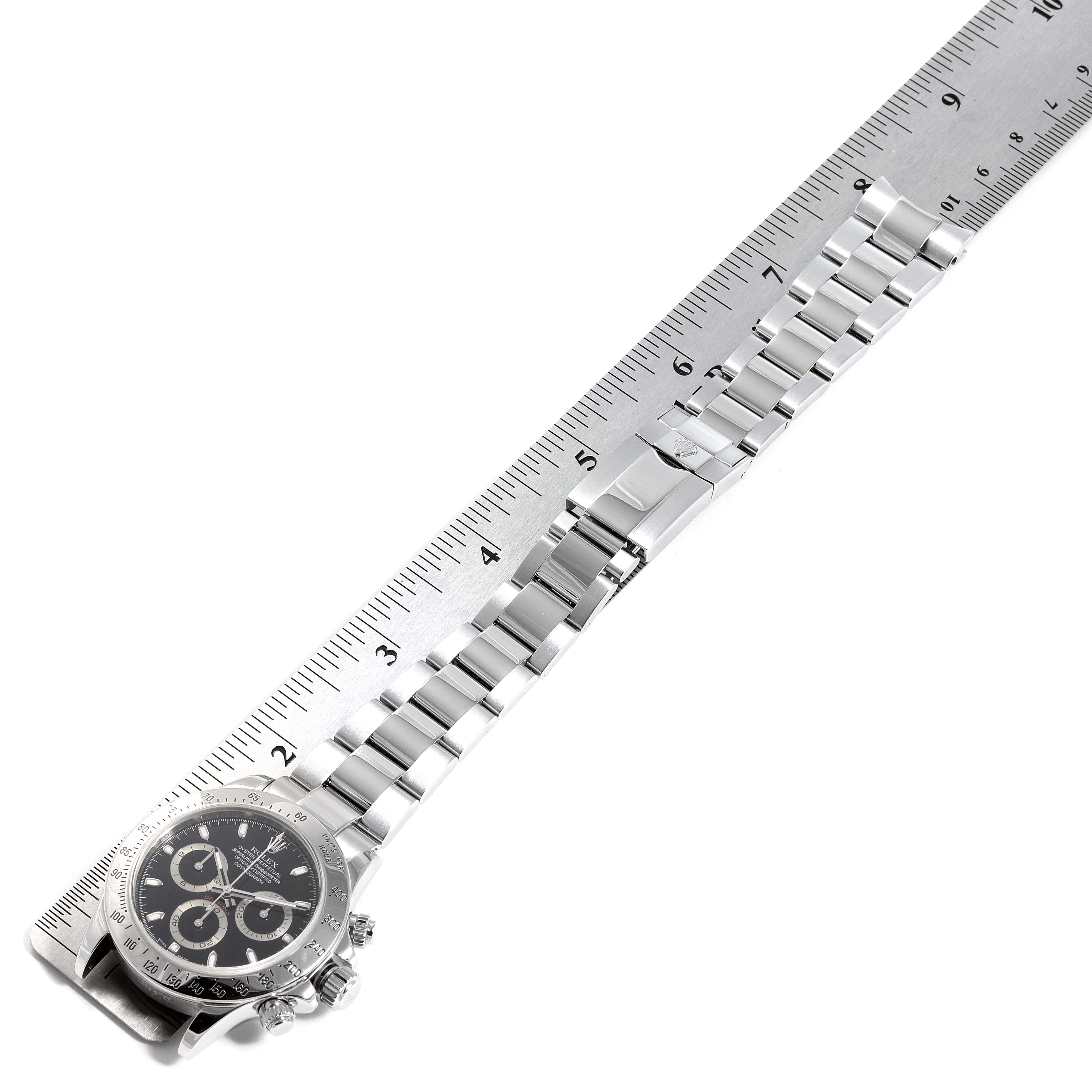 The image shows a Rolex Daytona 116520 Men's Stainless Steel Black Dial 116520 Men's Stainless Steel Black Dial watch laid flat with a ruler, displaying its bracelet and face at an angle.