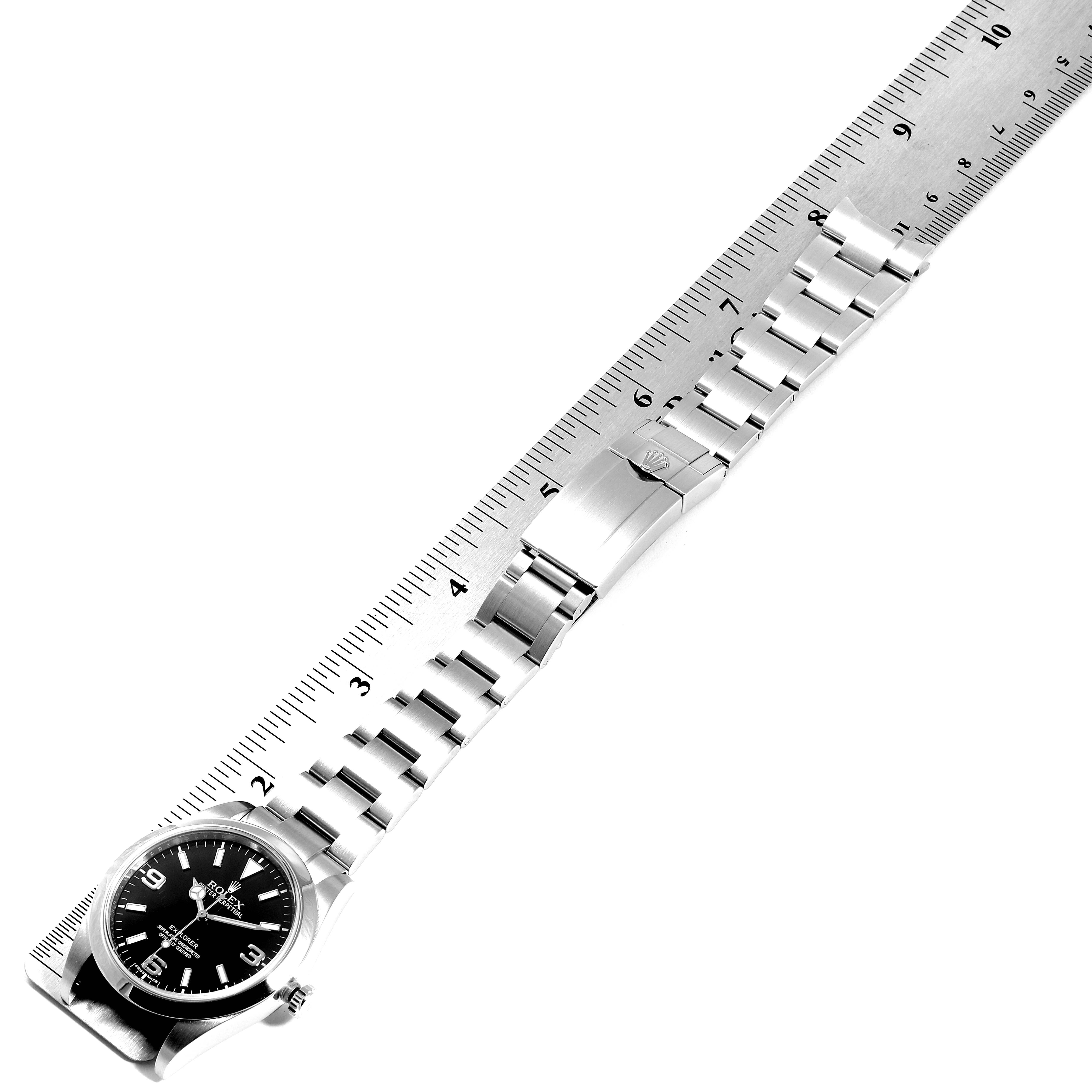 The Rolex Explorer 214270 Men
s Stainless Steel Black Dial 214270 Men
s Stainless Steel Black Dial watch is displayed flat against a ruler, showing its full dial and bracelet in a diagonal angle.