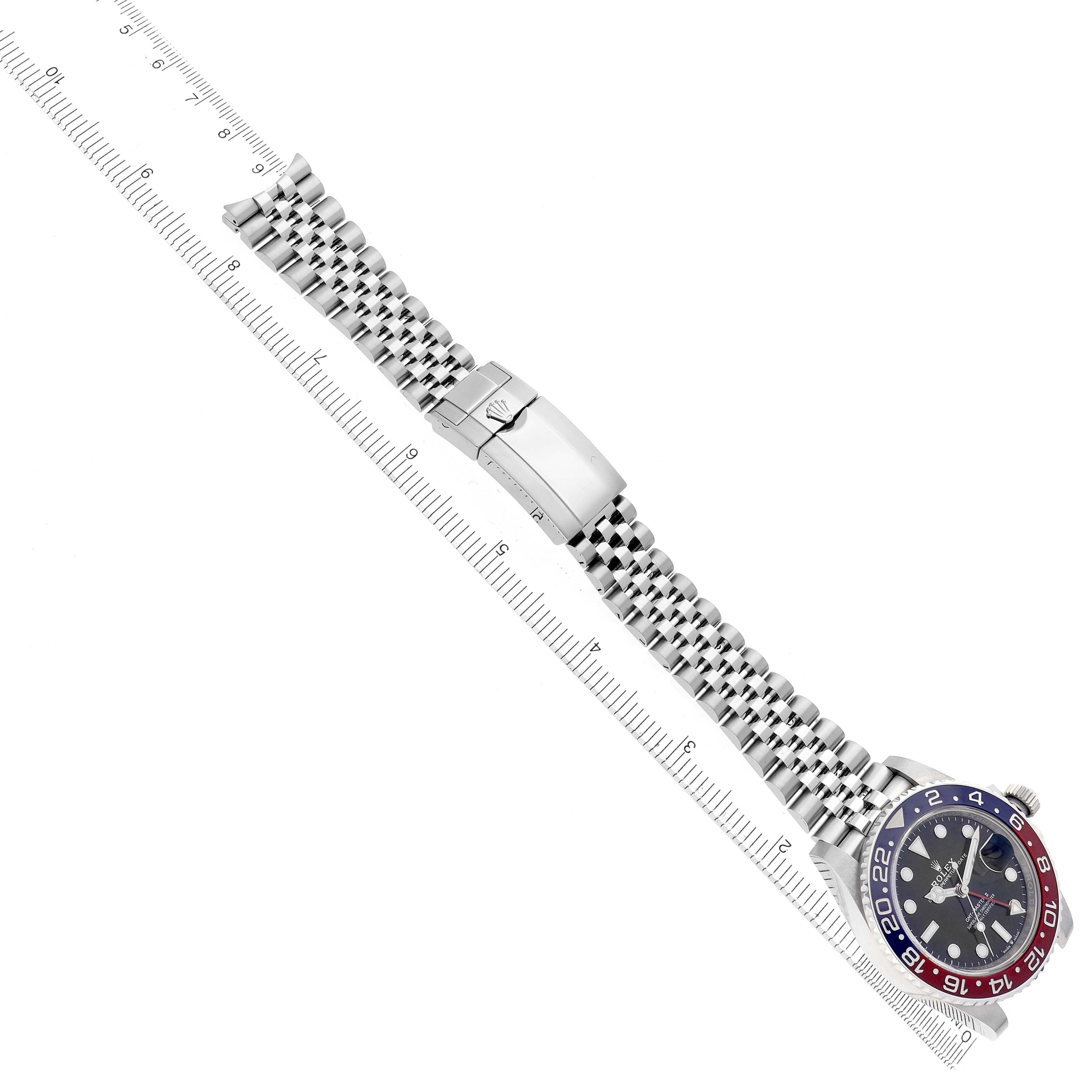 The image shows the Rolex GMT-Master 126710BLRO watch at a diagonal angle, highlighting its bracelet, clasp, and bezel alongside a measuring ruler.