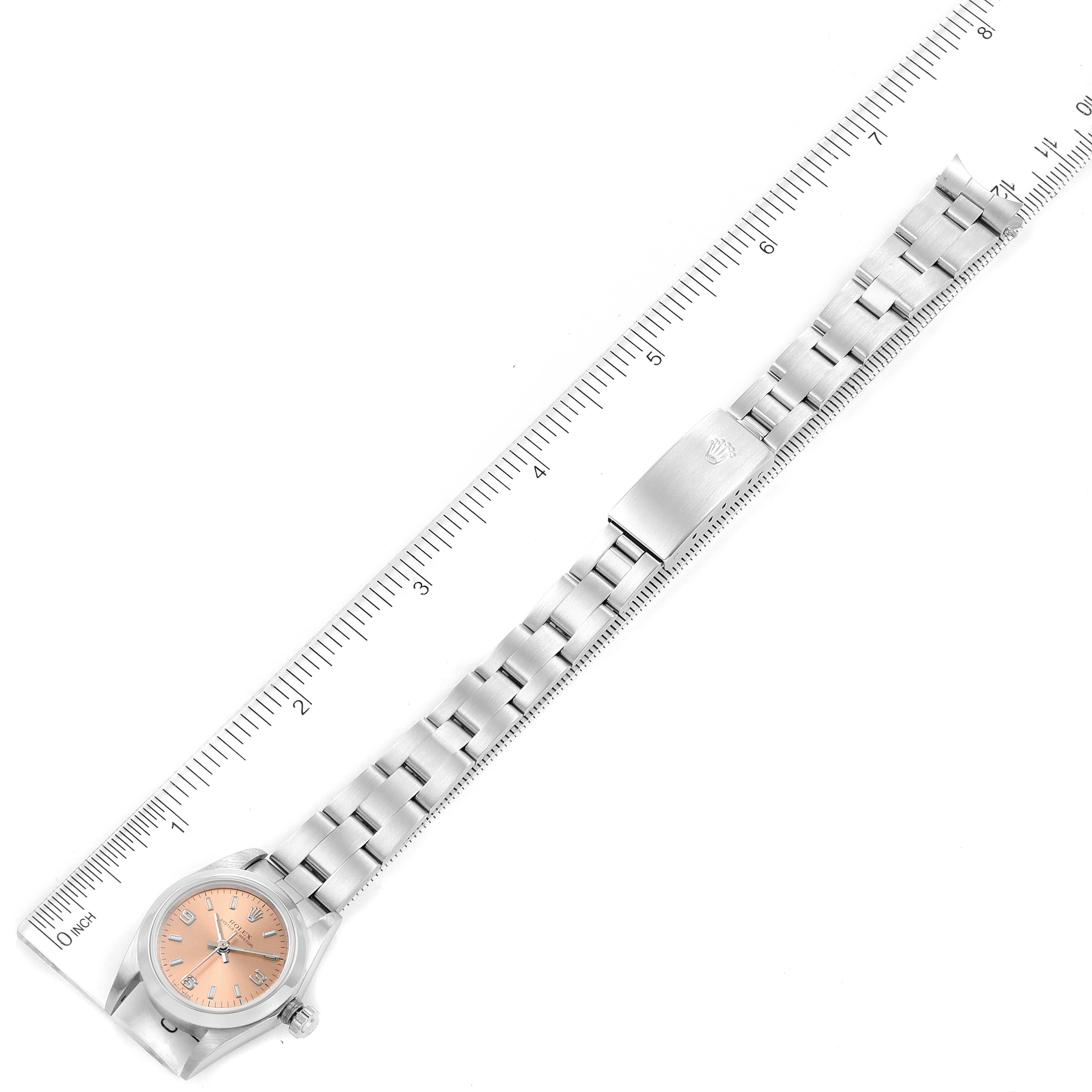 This image shows an overhead view of a Rolex Oyster Perpetual 76080 Women's Stainless Steel Pink Dial 76080 Women's Stainless Steel Pink Dial watch, including the entire watch face, band, and clasp, alongside a ruler for scale.