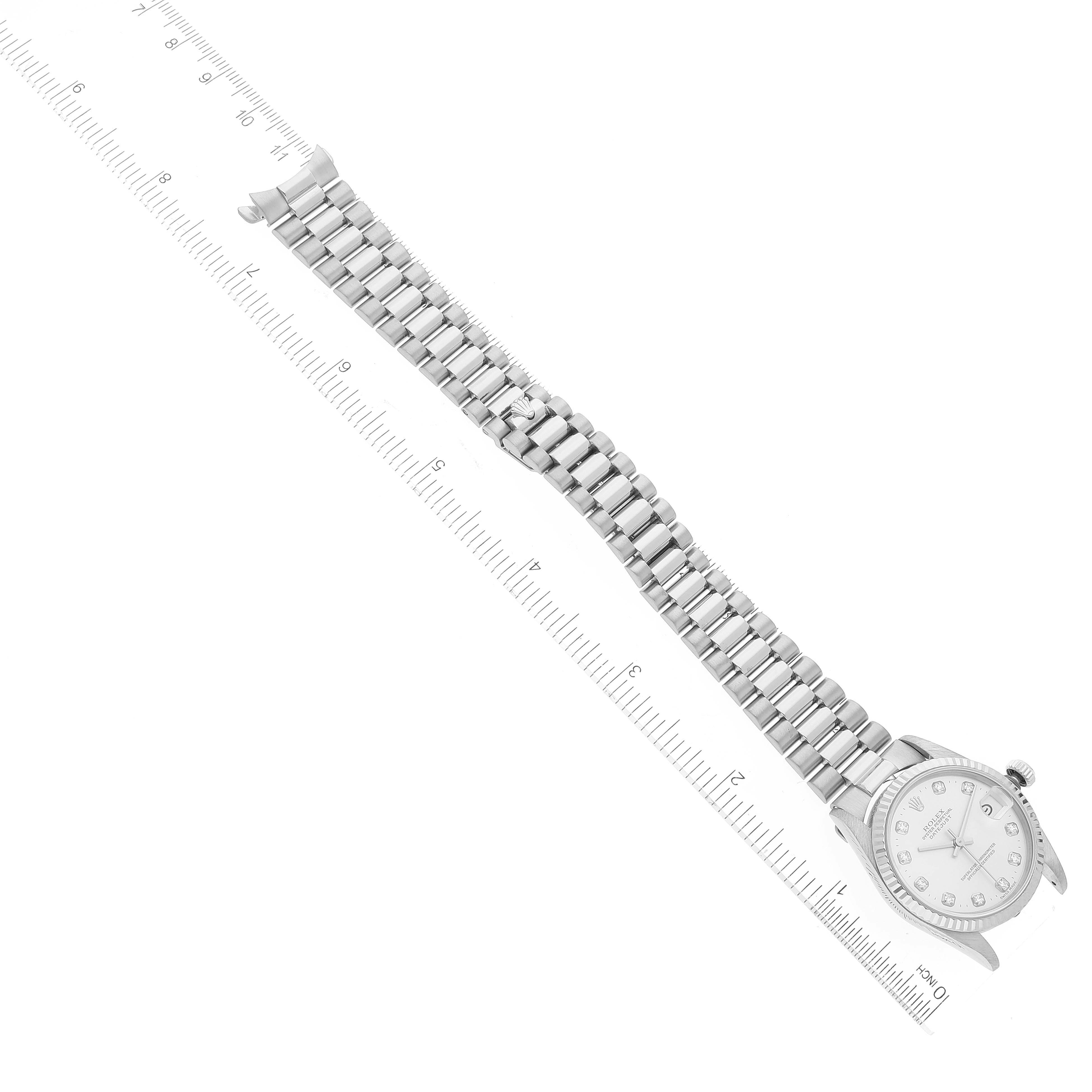 The image shows a Rolex President 68279 Women's White Gold Silver Dial 68279 Women's White Gold Silver Dial model watch with a stainless steel bracelet and diamond dial, lying diagonally with a ruler for scale.