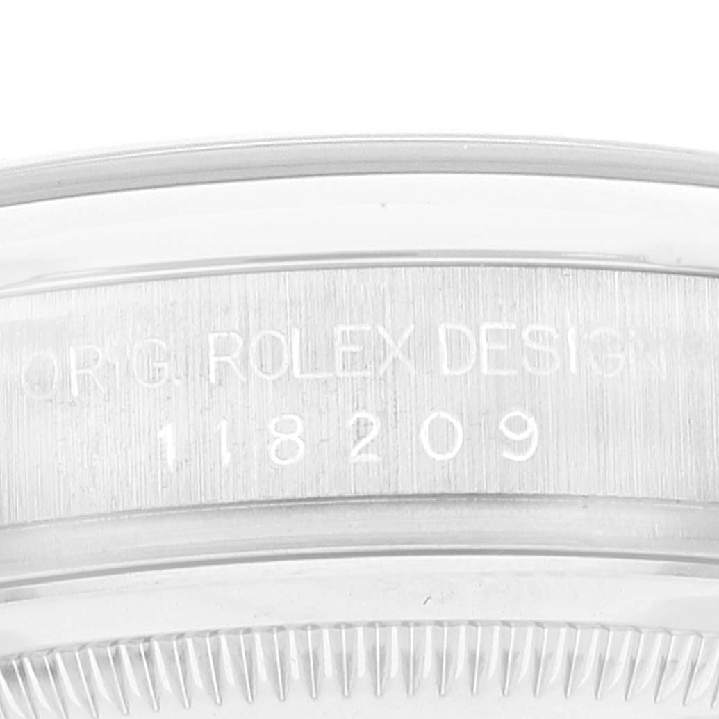 This close-up image of a Rolex President 118209 Men's White Gold Silver Dial 118209 Men's White Gold Silver Dial model watch shows the engraved serial and model numbers on the side of its case.