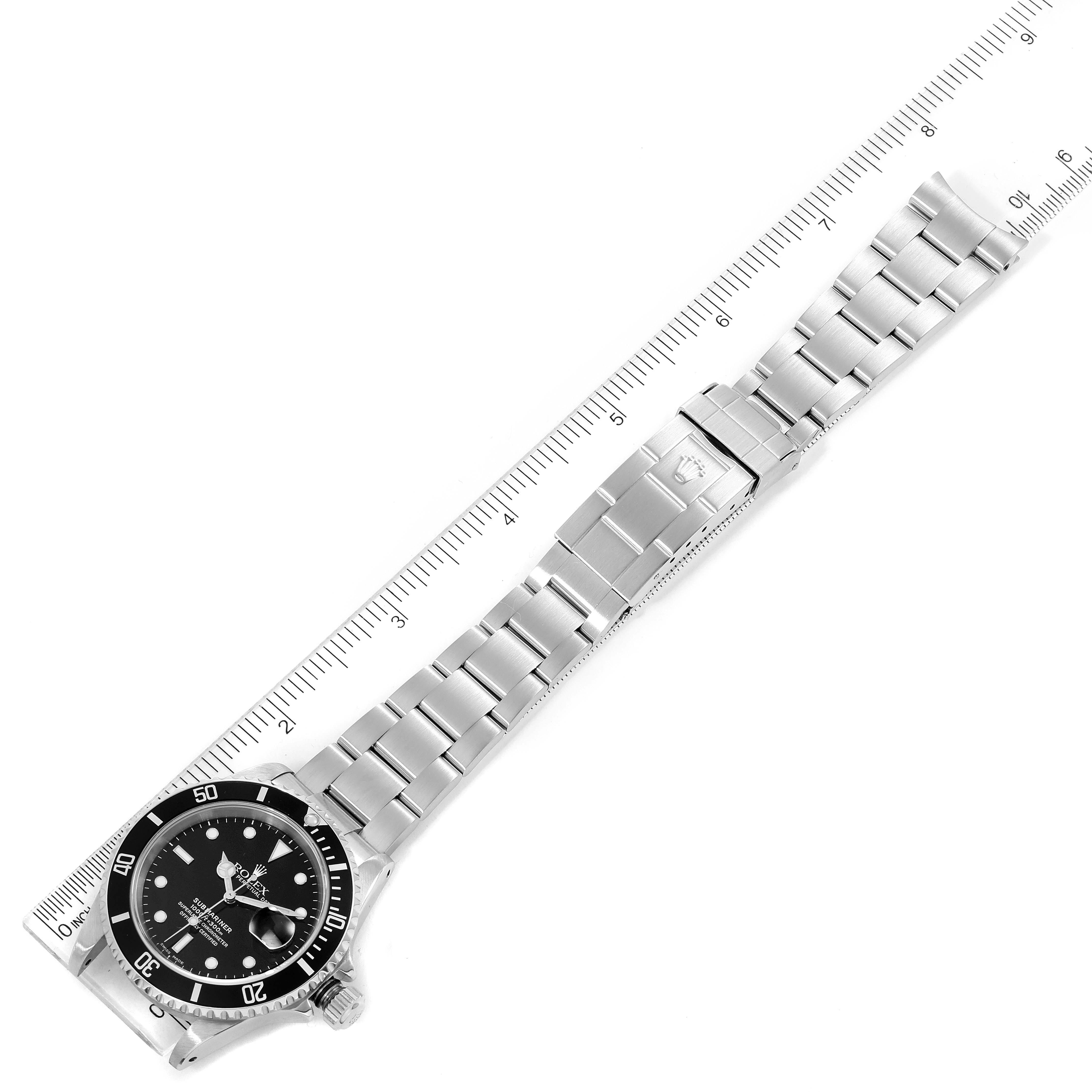 The image shows a Rolex Submariner 16610 Men
s Stainless Steel Black Dial 16610 Men
s Stainless Steel Black Dial watch laid flat with a fully extended metal bracelet adjacent to a ruler.