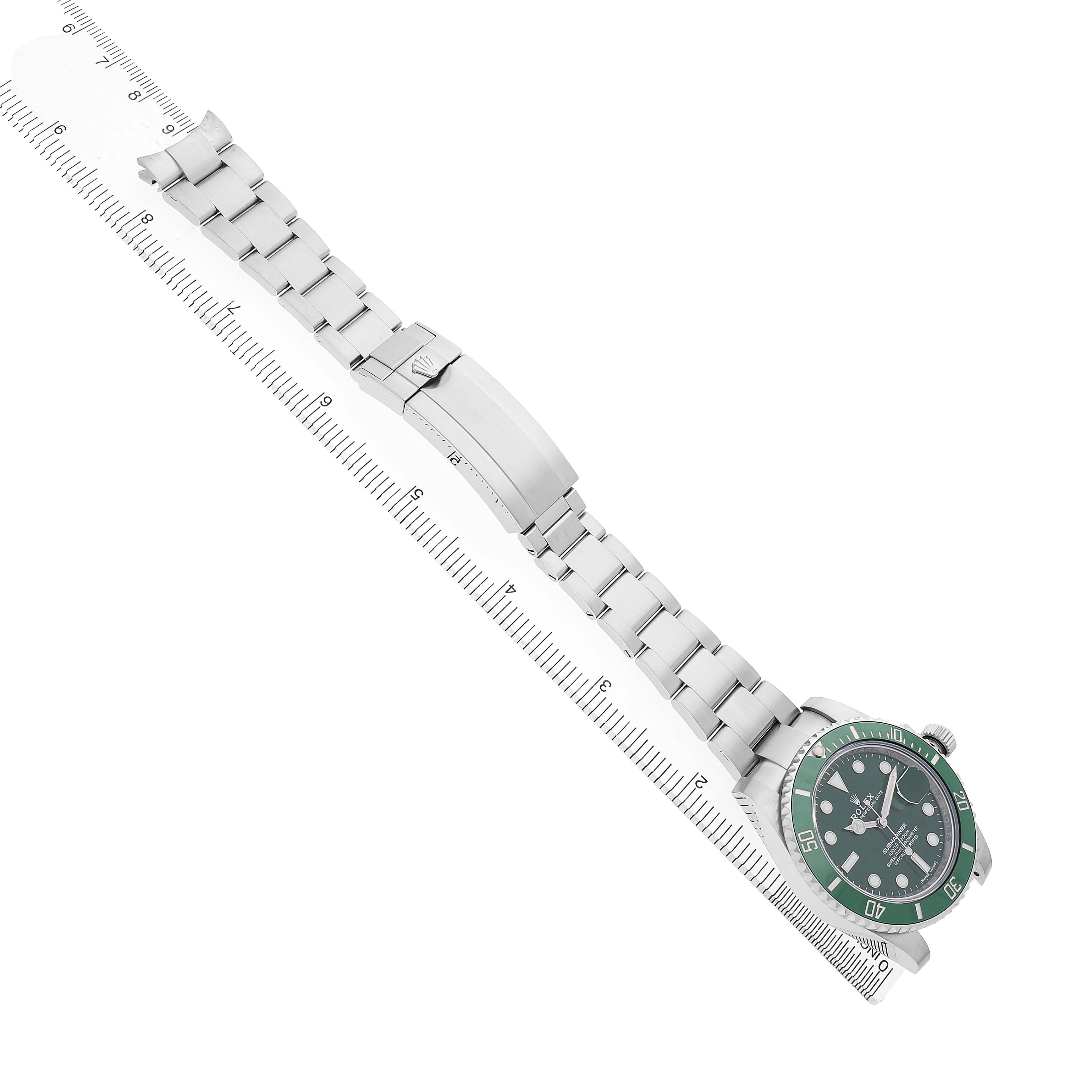 The Rolex Submariner 116610LV Men's Stainless Steel Green Dial is shown from an angled top view, displaying the green bezel, dial, and full bracelet alongside a ruler.