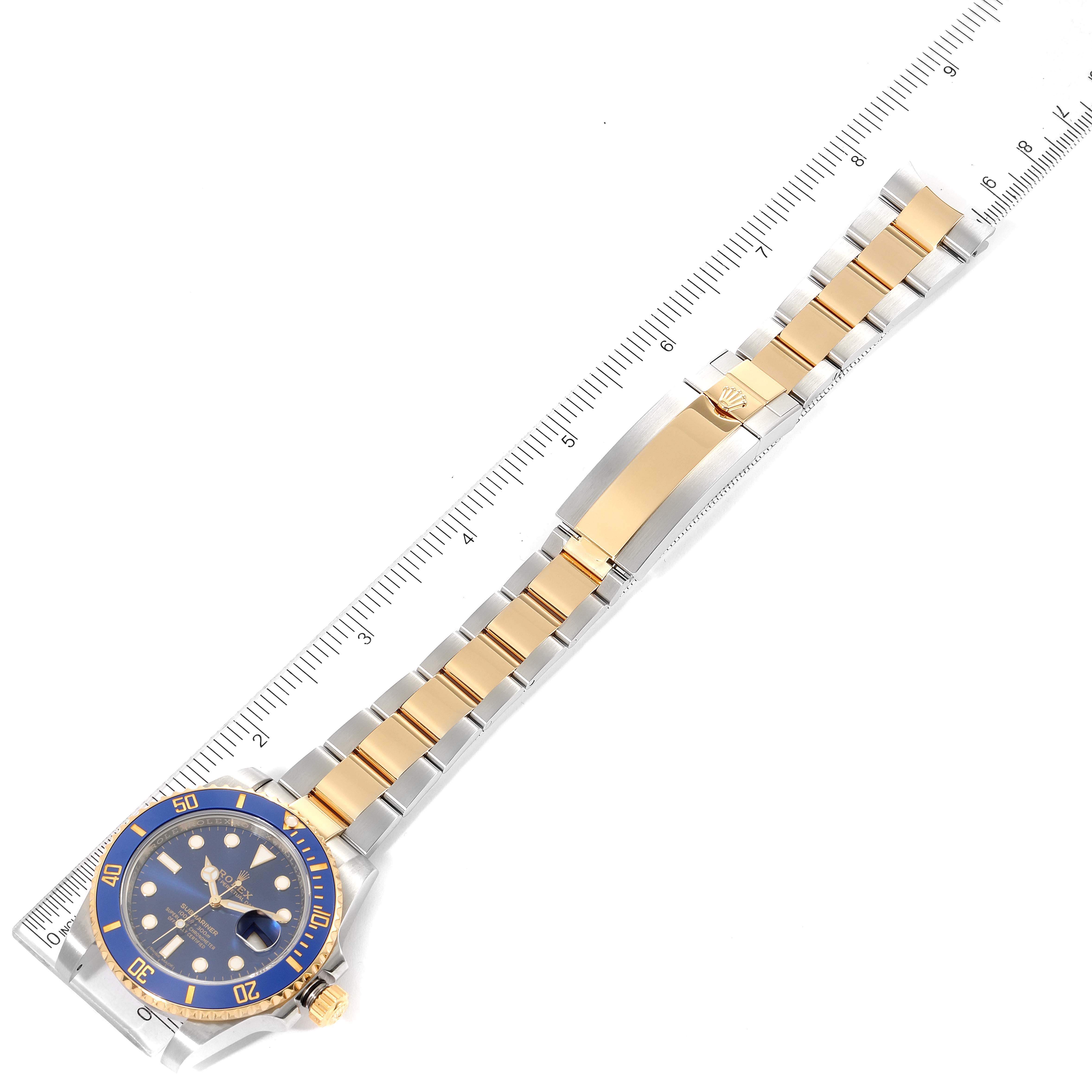 The image shows a top-down view of the Rolex Submariner 116613 Men
s Steel and Gold (two tone) Blue Dial 116613 Men
s Steel and Gold (two tone) Blue Dial watch, highlighting its blue dial, bezel, and two-tone metal bracelet next to a ruler.