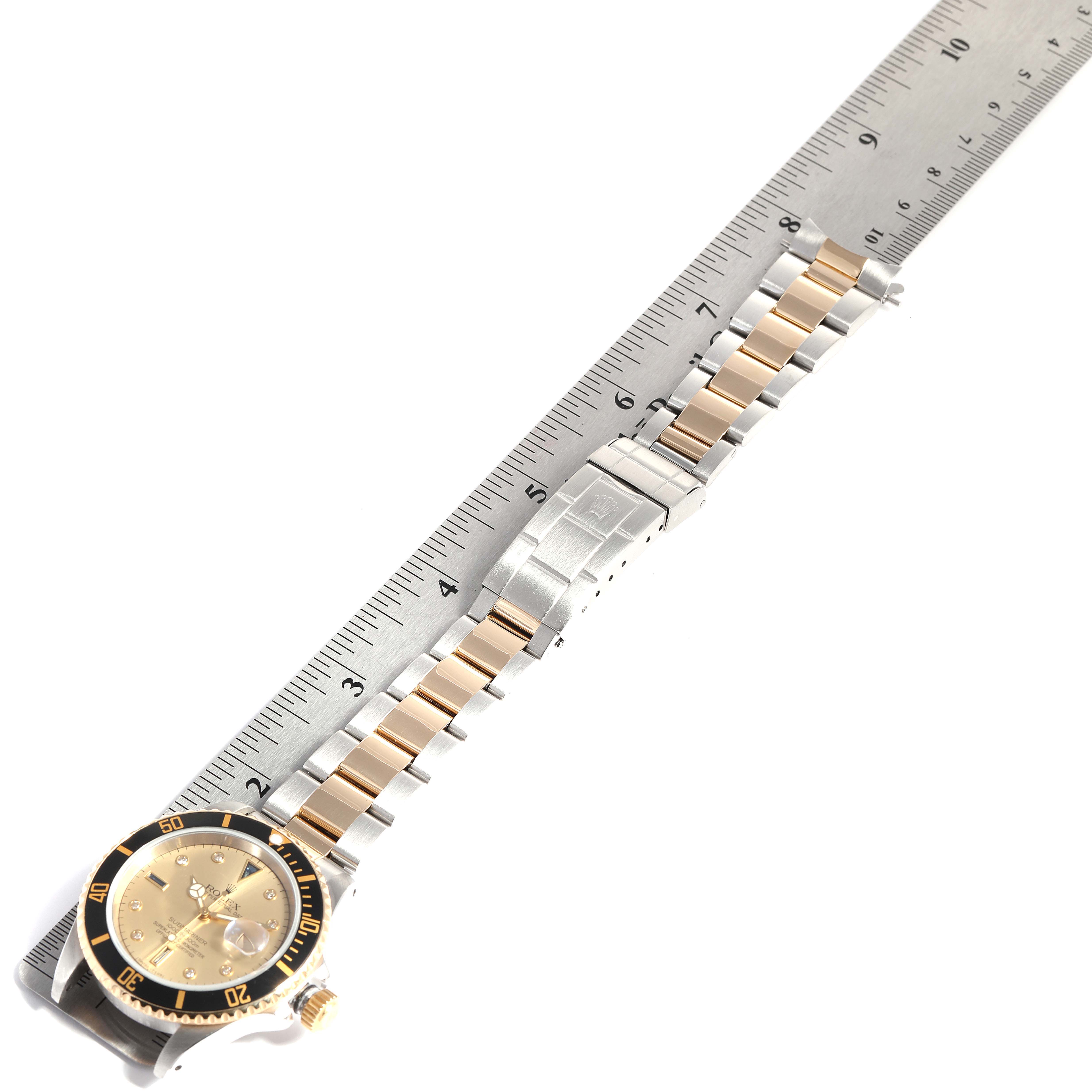 The image shows the face, bezel, and full bracelet of the Rolex Submariner 16613 Men
s Steel and Gold (two tone) Champagne Dial 16613 Men
s Steel and Gold (two tone) Champagne Dial watch, placed diagonally alongside a ruler.