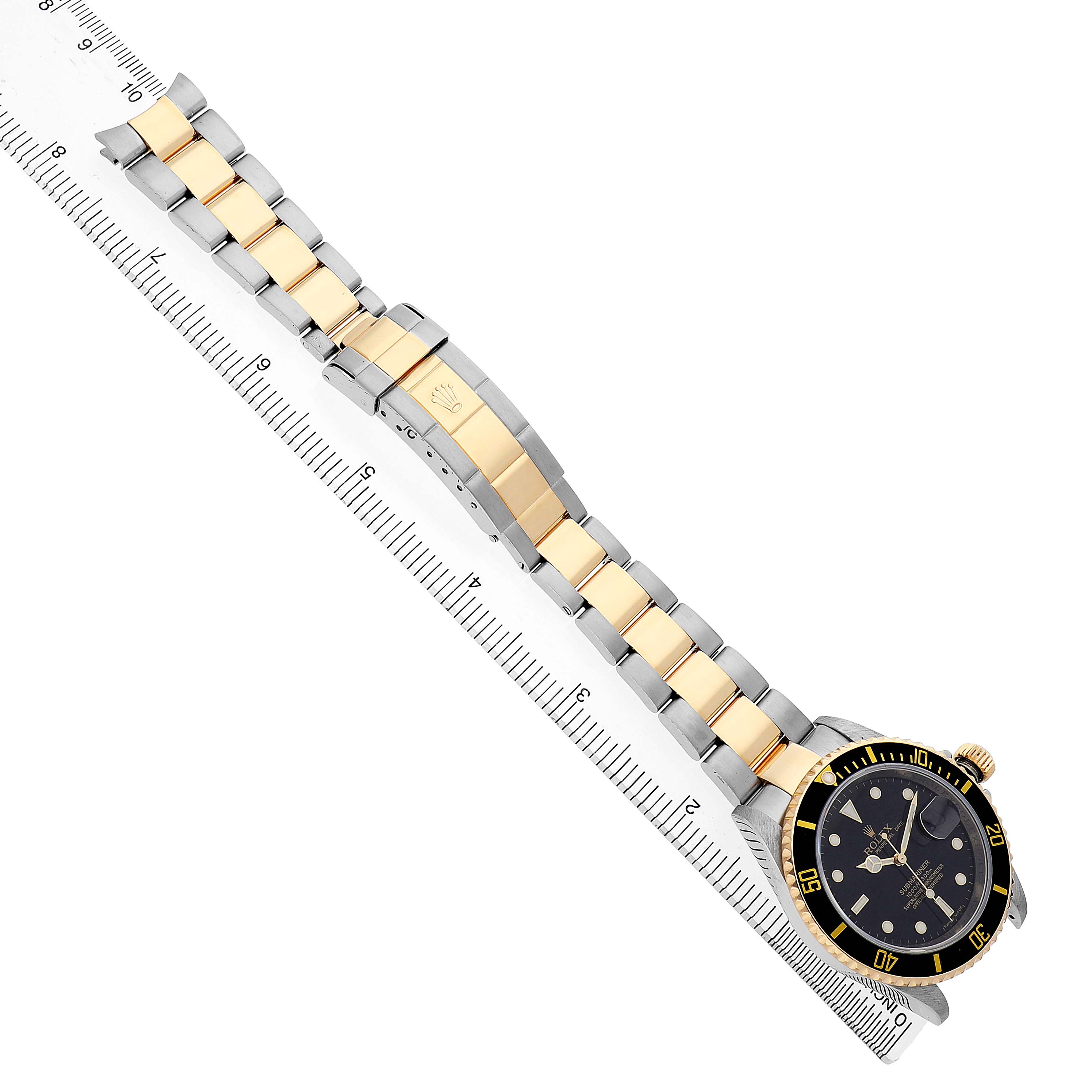 The Rolex Submariner 16613LN Men's Steel and Gold (two tone) Black Dial watch is shown from an overhead angle, highlighting its two-tone bracelet and bezel next to a ruler.