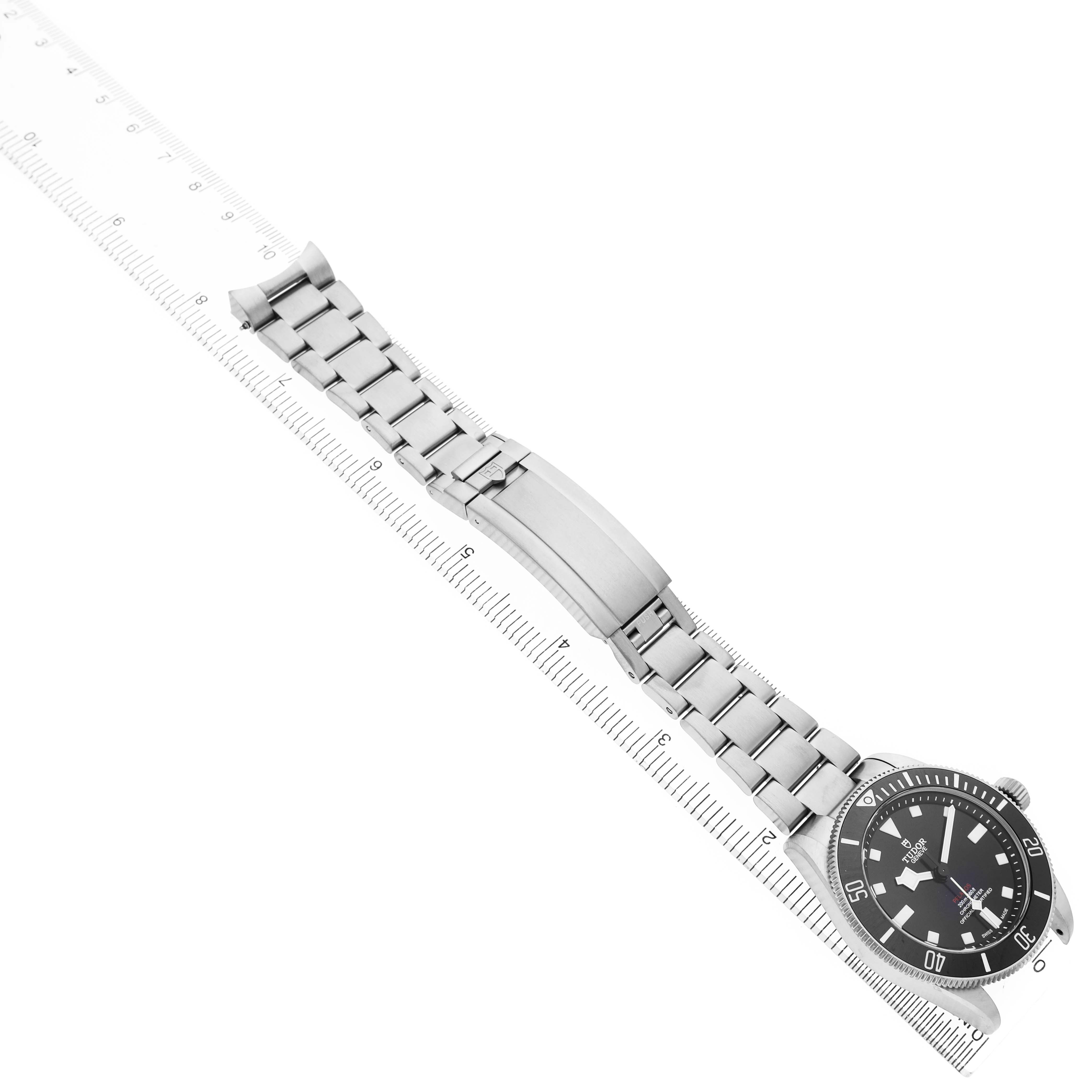 The Tudor Pelagos M25407N Men's Titanium Black Dial watch is shown from an angled side view, highlighting the face, bezel, and bracelet clasp placed on a ruler.