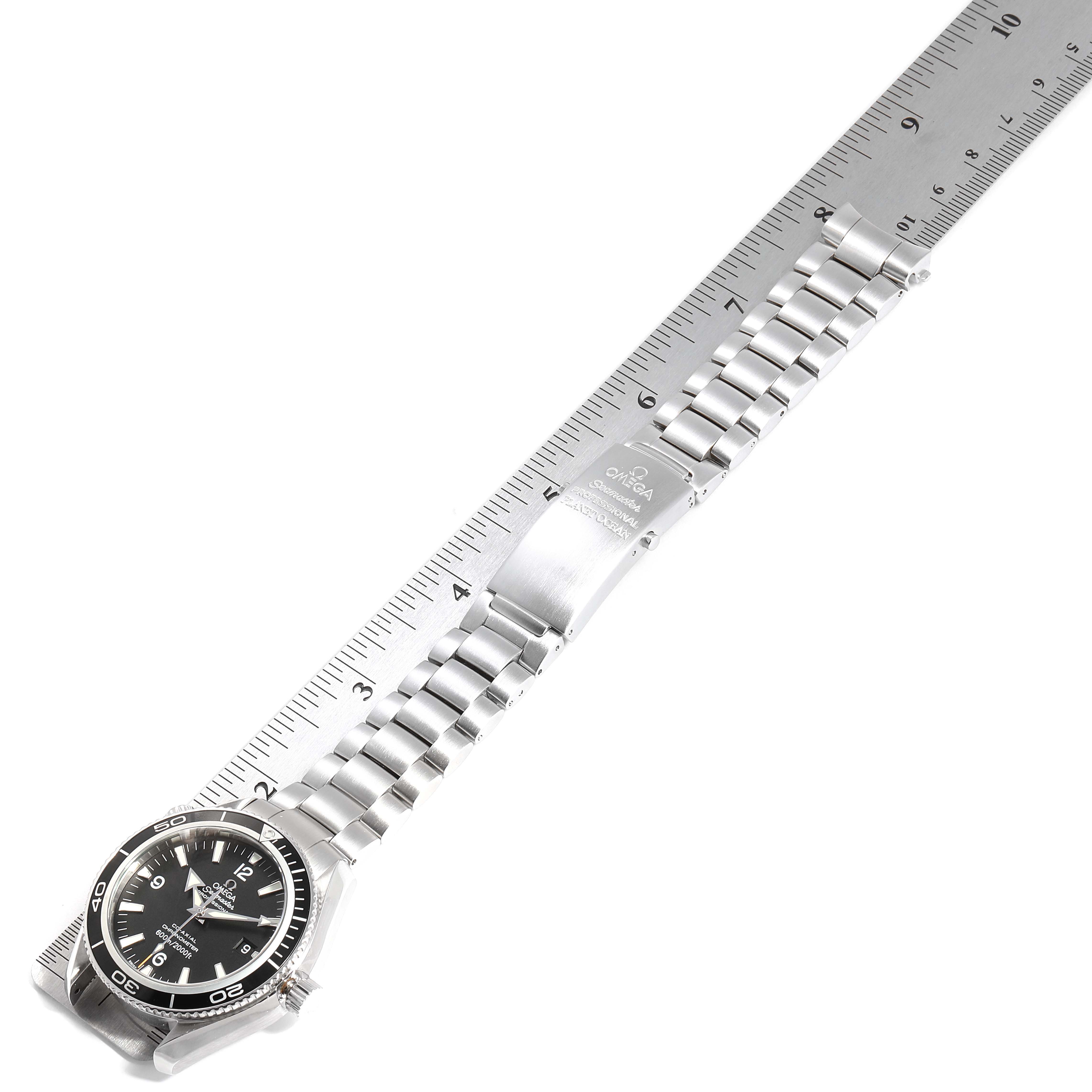 The image shows an Omega Planet Ocean 2201.50.00 Men
s Stainless Steel Black Dial 2201.50.00 Men
s Stainless Steel Black Dial watch laid flat, displaying the face, bracelet, and clasp against a ruler for size reference.