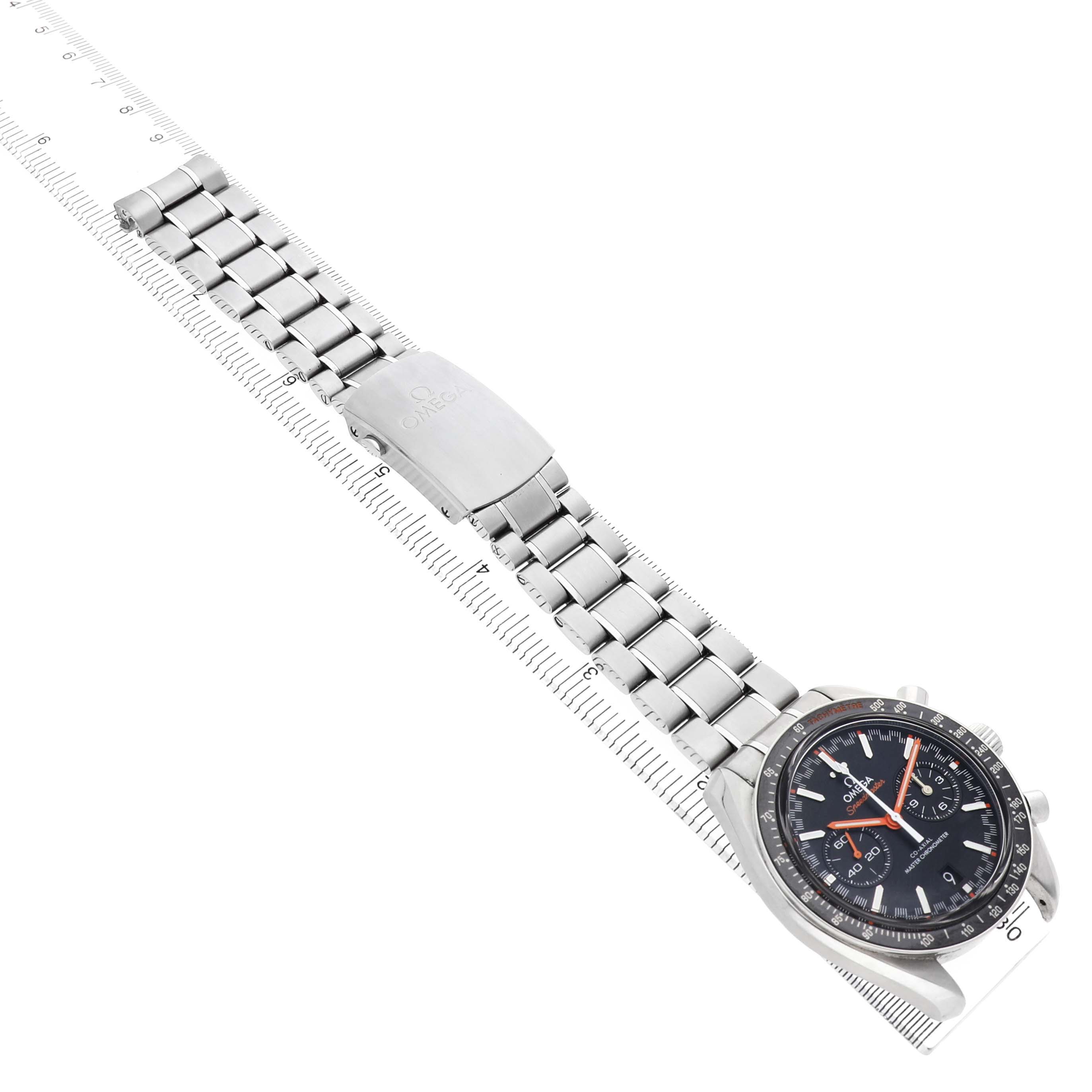 The Omega Speedmaster 329.30.44.51.01.002 Men's Stainless Steel Black Dial watch is shown from a top angle, highlighting the face, bracelet, and clasp, positioned alongside a measuring ruler.
