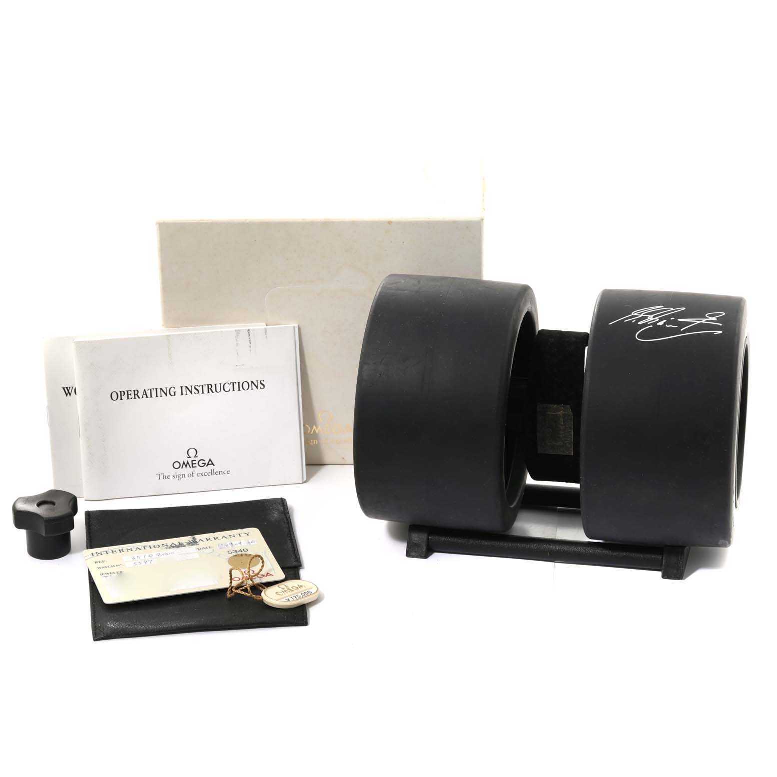 The image shows accessories for an Omega Speedmaster 3510.80.00 Men's Stainless Steel Blue Dial 3510.80.00 Men's Stainless Steel Blue Dial watch, including the operating instructions, box, tags, and a unique cylindrical case.