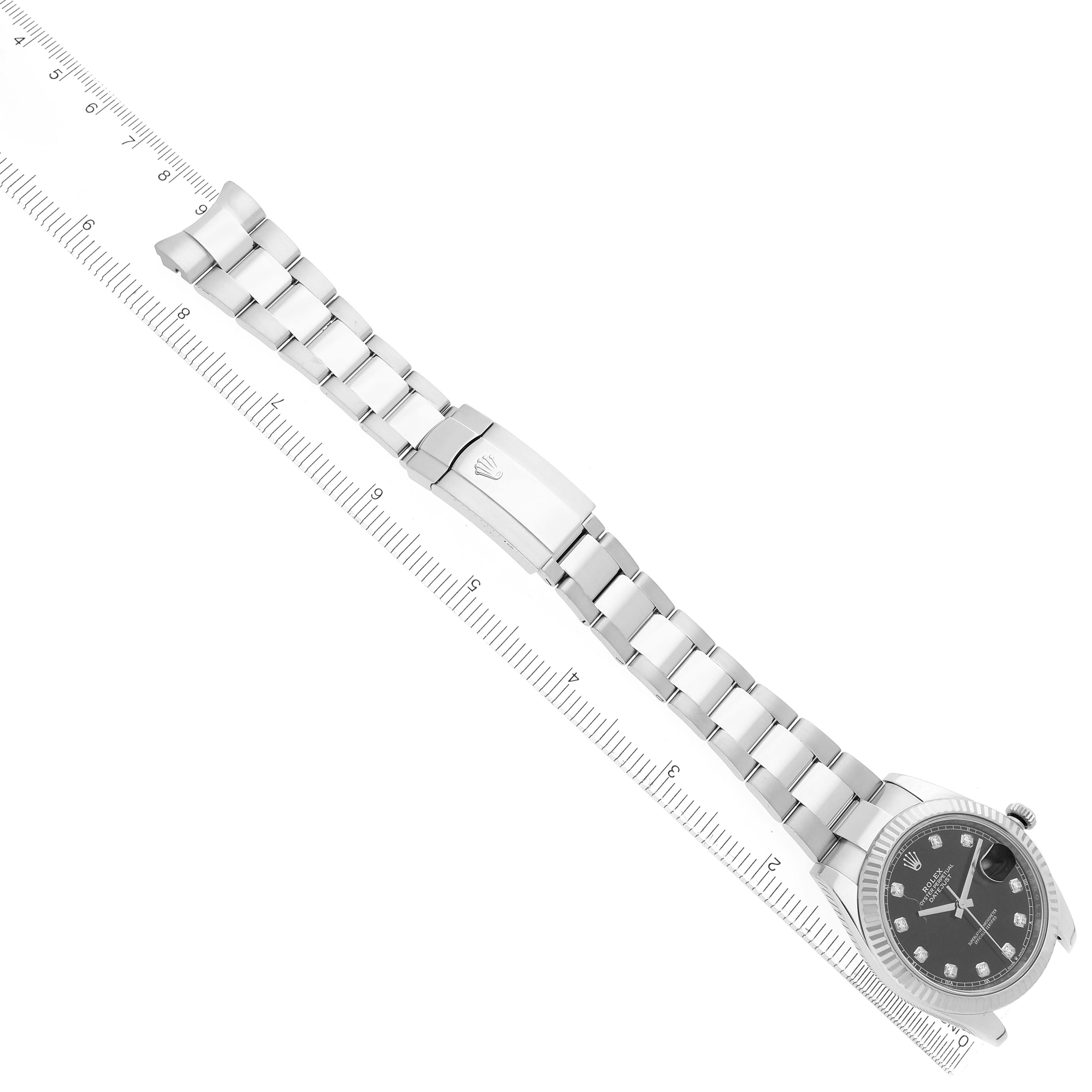 The Rolex Datejust watch is shown from a top angle, displaying the full bracelet, clasp, and dial beside a ruler for scale.
