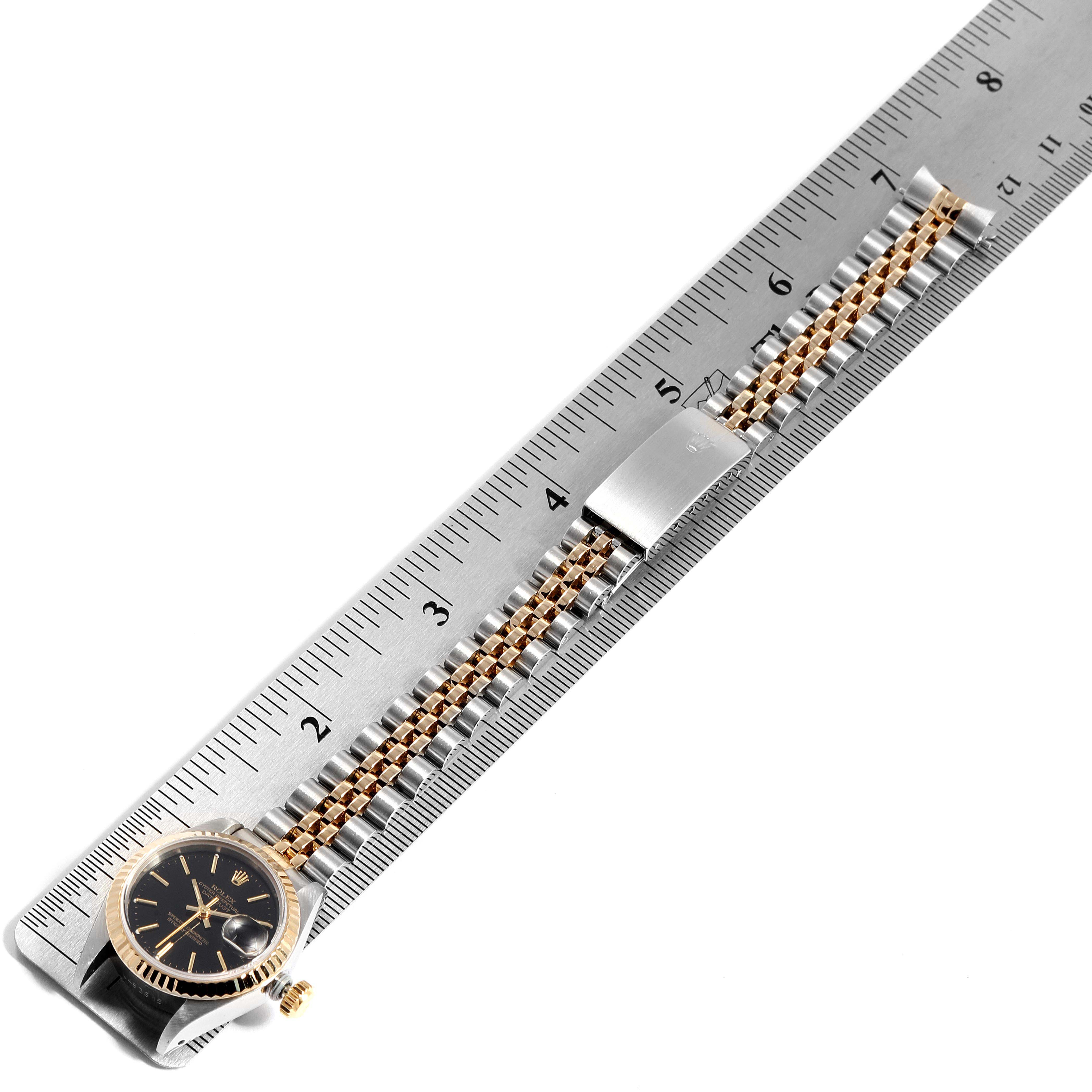 The image shows a Rolex Datejust 69173 Women
s Steel and Gold (two tone) Black Dial 69173 Women
s Steel and Gold (two tone) Black Dial model watch lying flat against a ruler, showcasing its dial and bracelet.