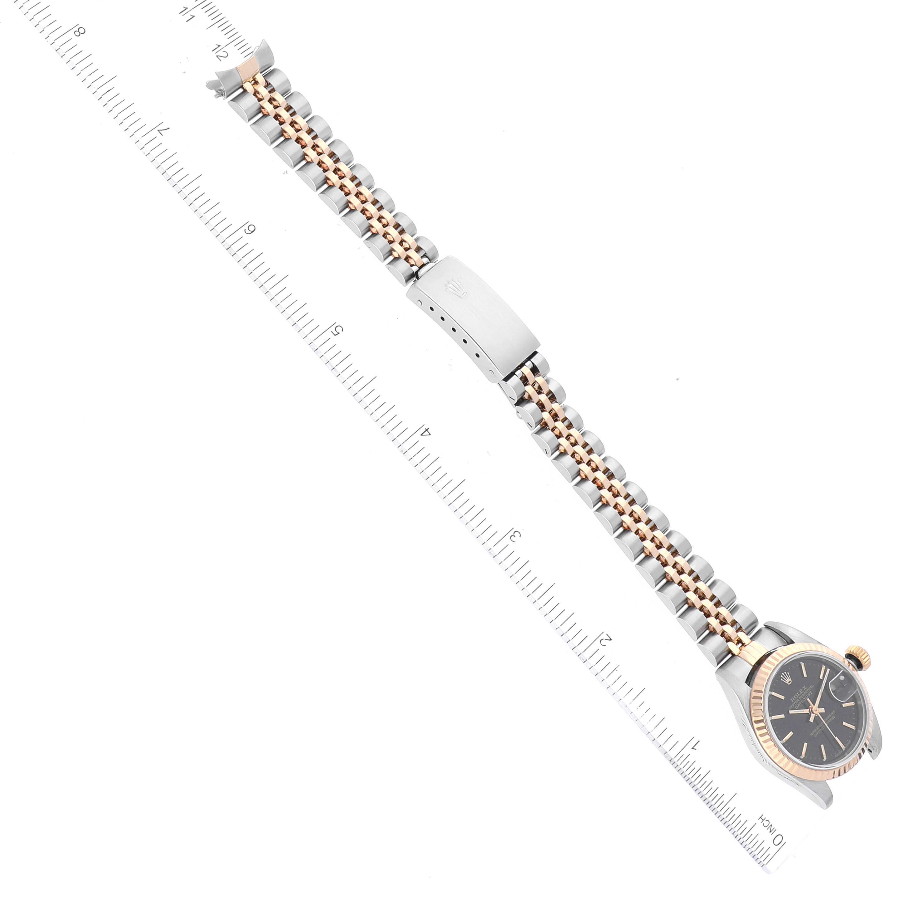 This image shows an aerial view of a Rolex Datejust 79173 Women's Steel and Gold (two tone) Black Dial 79173 Women's Steel and Gold (two tone) Black Dial watch with a two-tone metal bracelet, featuring a clasp and a ruler for scale.