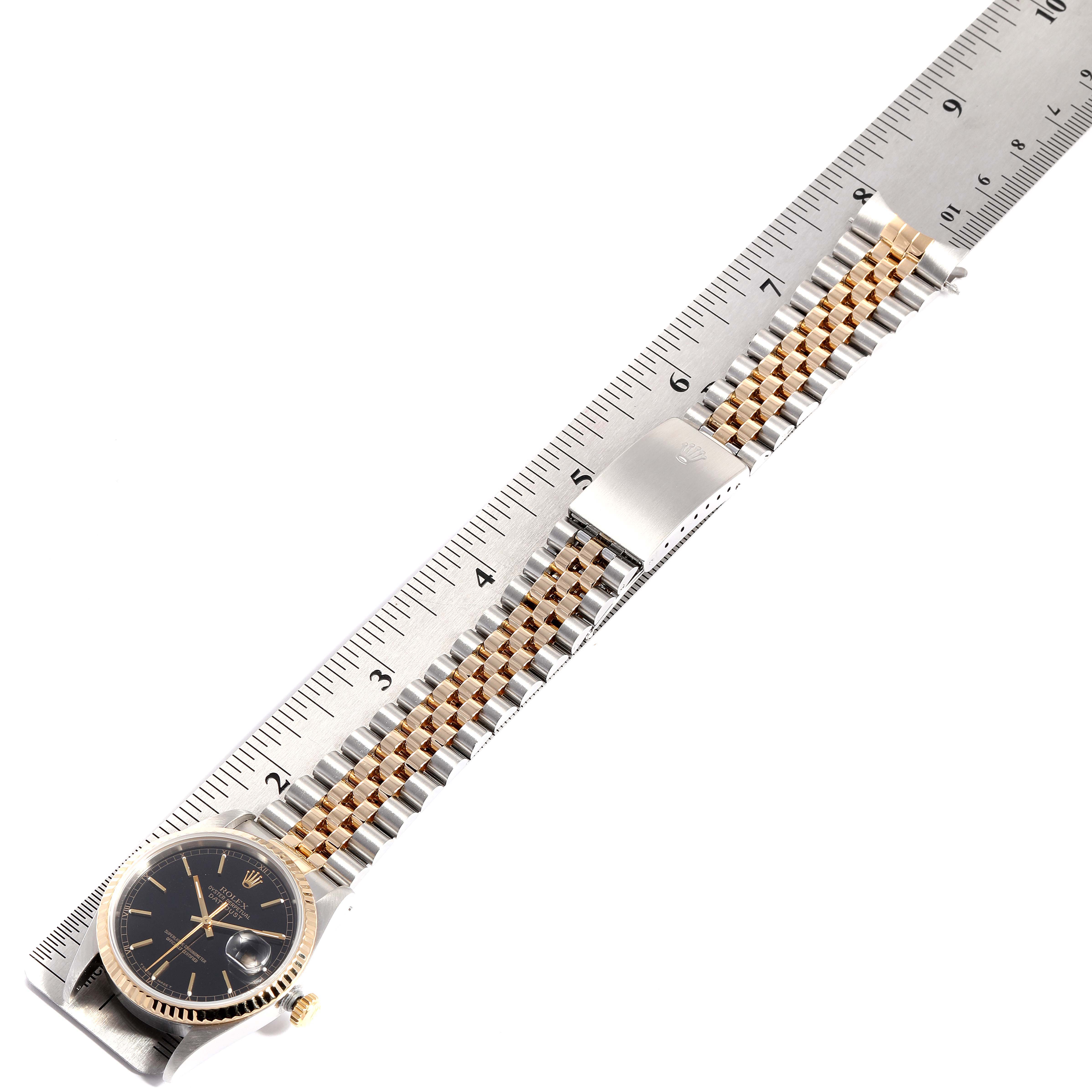 This image shows a Rolex Datejust 16233 Men
s Steel and Gold (two tone) Black Dial 16233 Men
s Steel and Gold (two tone) Black Dial model watch lying flat with its dial, bezel, and bracelet aligned to a ruler.