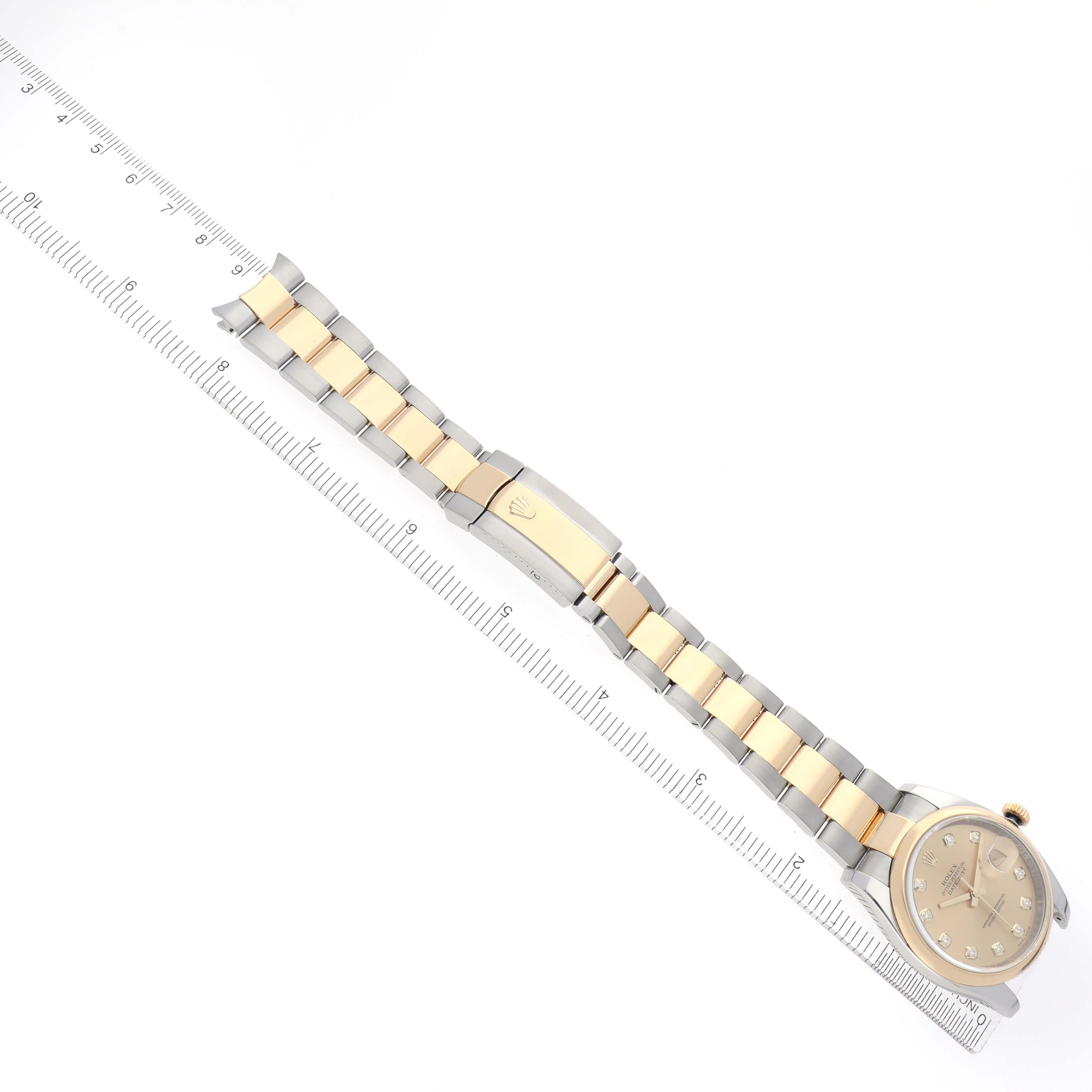 The Rolex Datejust 116203 Men
s Steel and Gold (two tone) Champagne Dial 116203 Men
s Steel and Gold (two tone) Champagne Dial watch is shown from a top view with its face, bracelet, and clasp fully visible alongside a ruler.