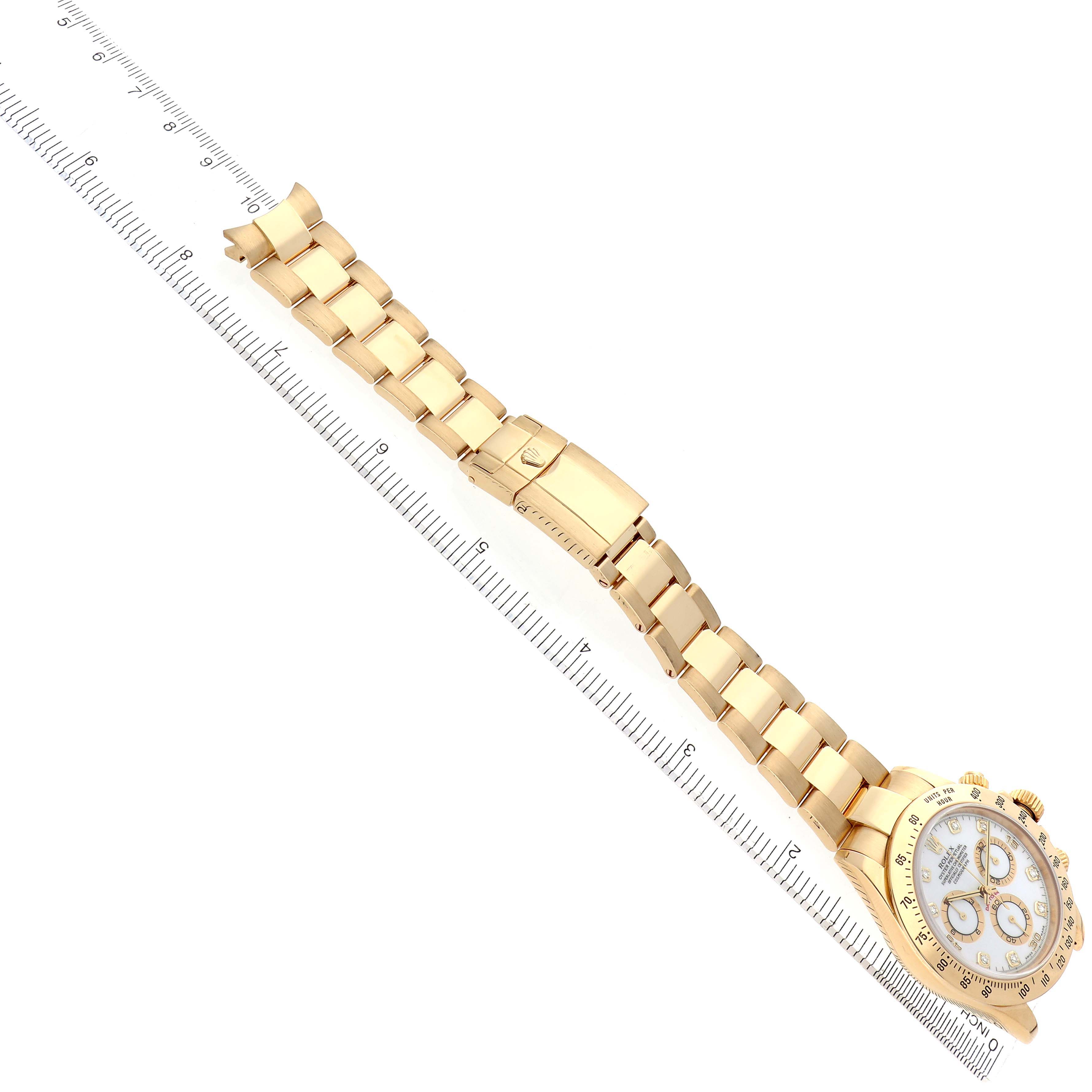 The Rolex Daytona 116528 Men
s Yellow Gold White Dial 116528 Men
s Yellow Gold White Dial watch is shown from a top view, displaying the full bracelet and closed clasp alongside a measuring ruler.