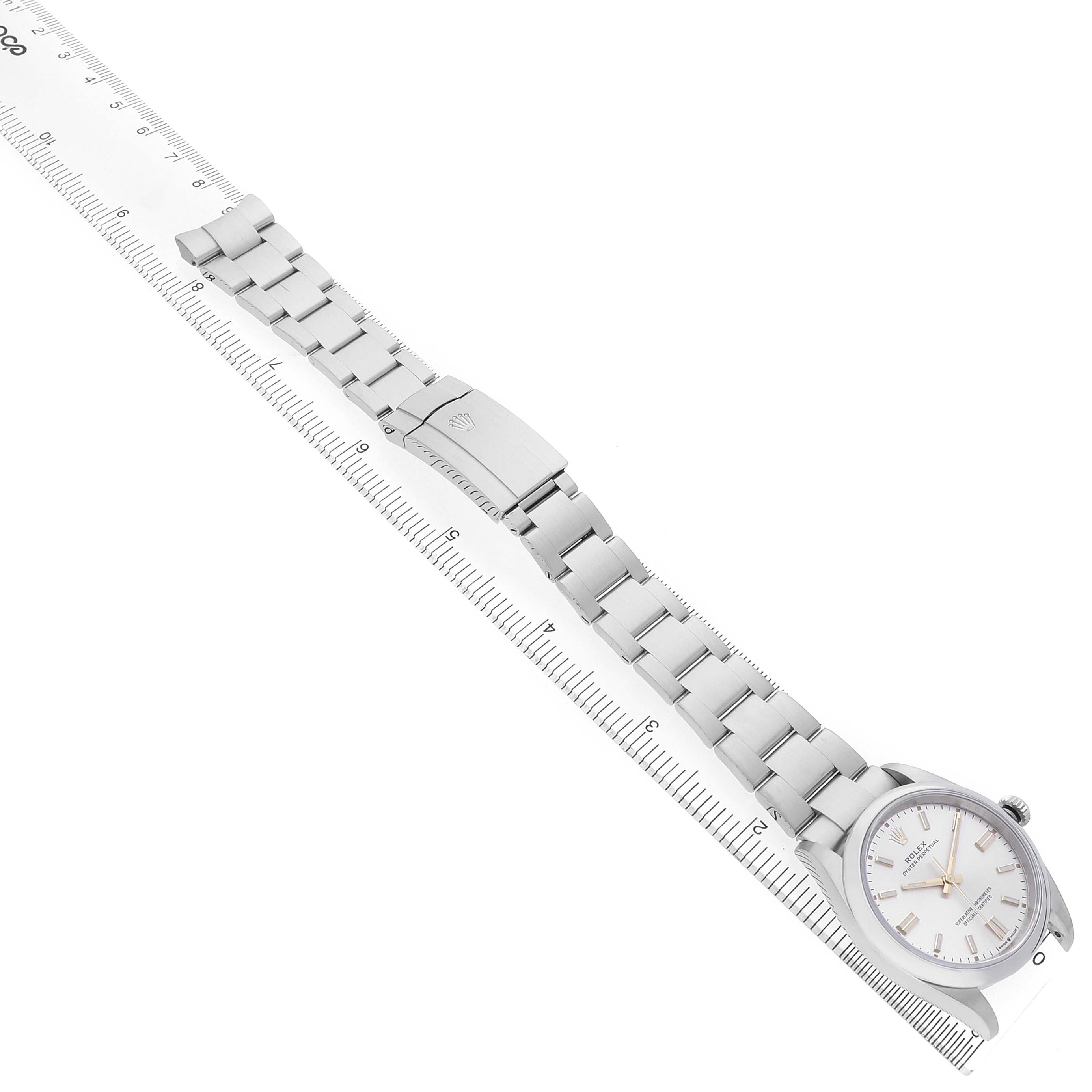 The Rolex Oyster Perpetual M126000-0001 Men's Stainless Steel Silver Dial watch is shown from a top-down angle, highlighting the face, bezel, and full bracelet alongside a ruler.