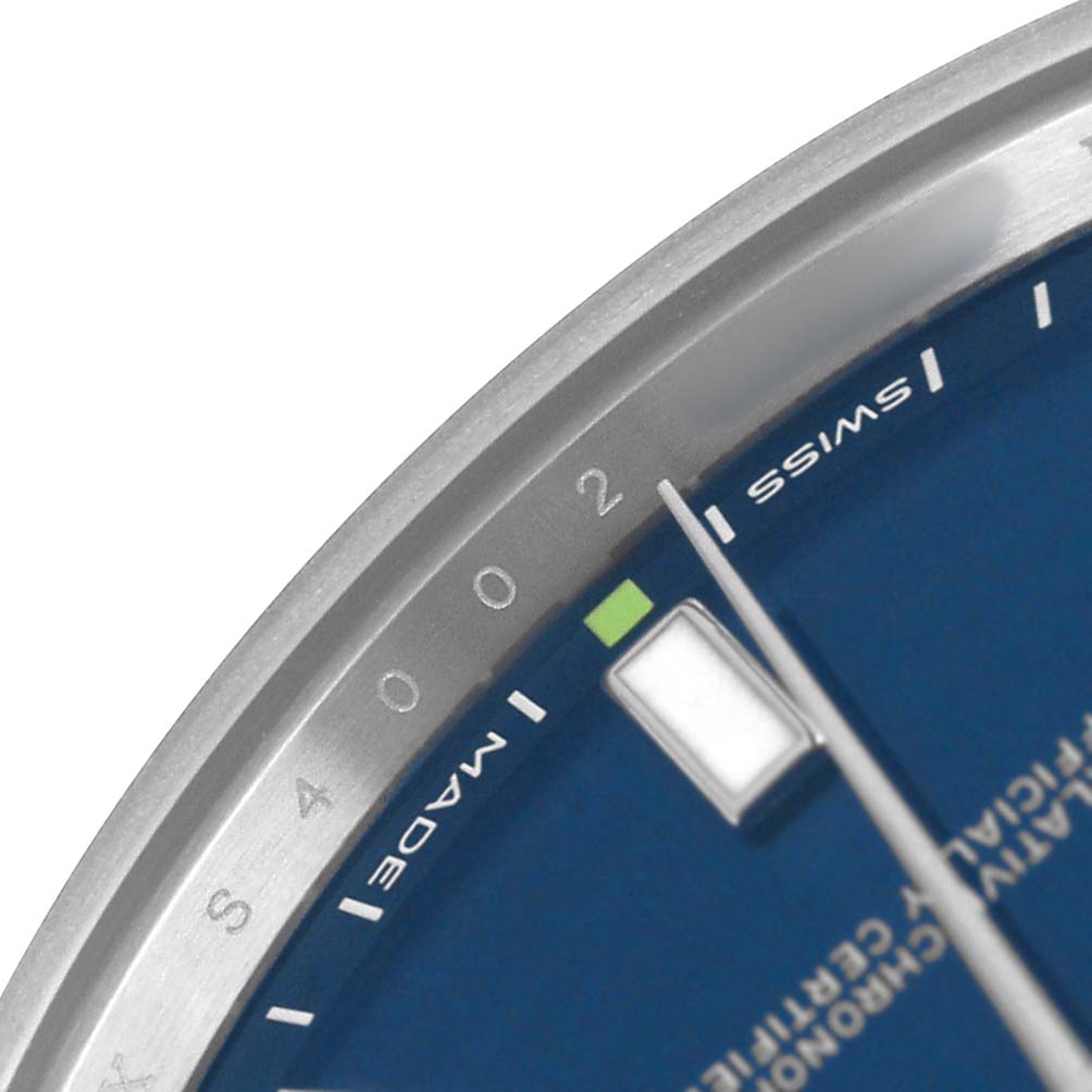 The image shows a close-up of the dial and bezel of a Rolex Oyster Perpetual 114300 Men's Stainless Steel Blue Dial watch, focusing on the minute markers and text.