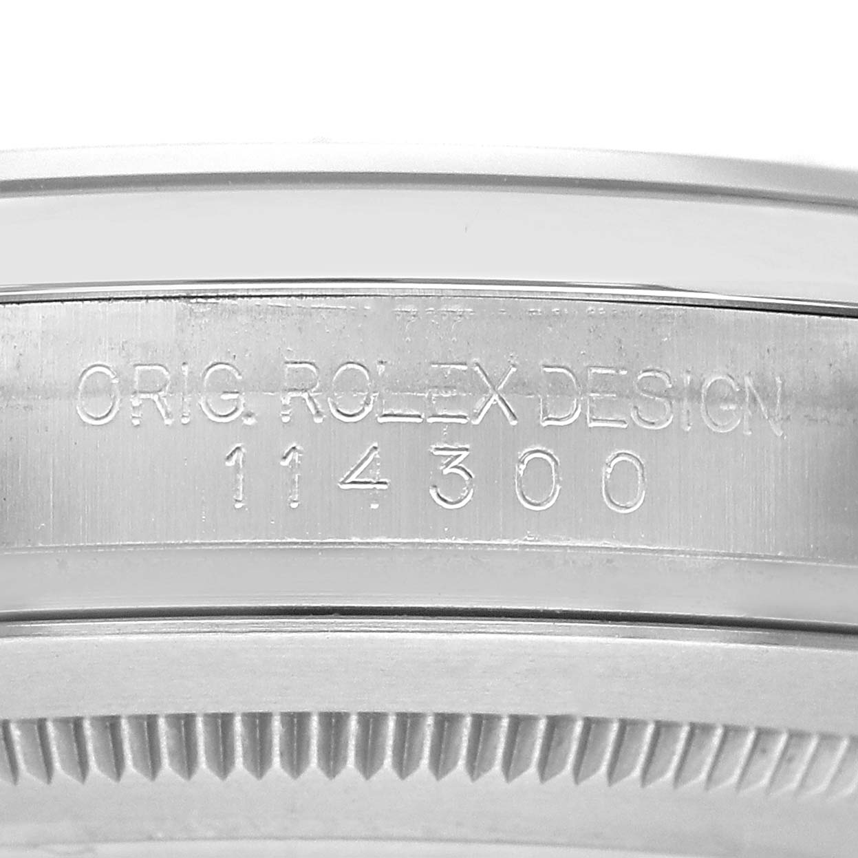 The image shows an angled view of the side of the Rolex Oyster Perpetual 114300 Men's Stainless Steel Blue Dial watch case, displaying the engraved model number and design details.