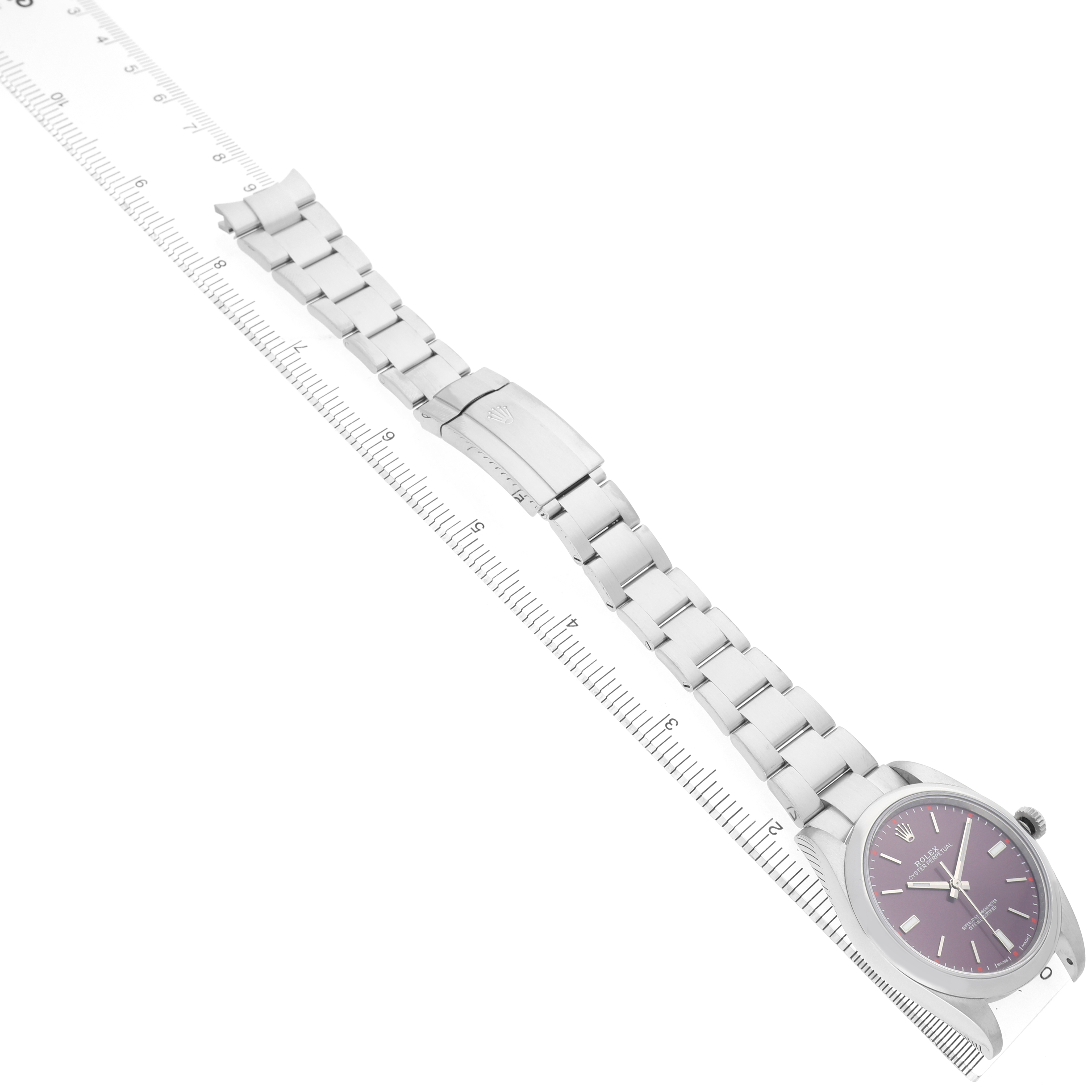 The Rolex Oyster Perpetual 114300 Men's Stainless Steel Purple Dial watch is shown diagonally, displaying the face, bracelet, and clasp, alongside a measuring ruler.
