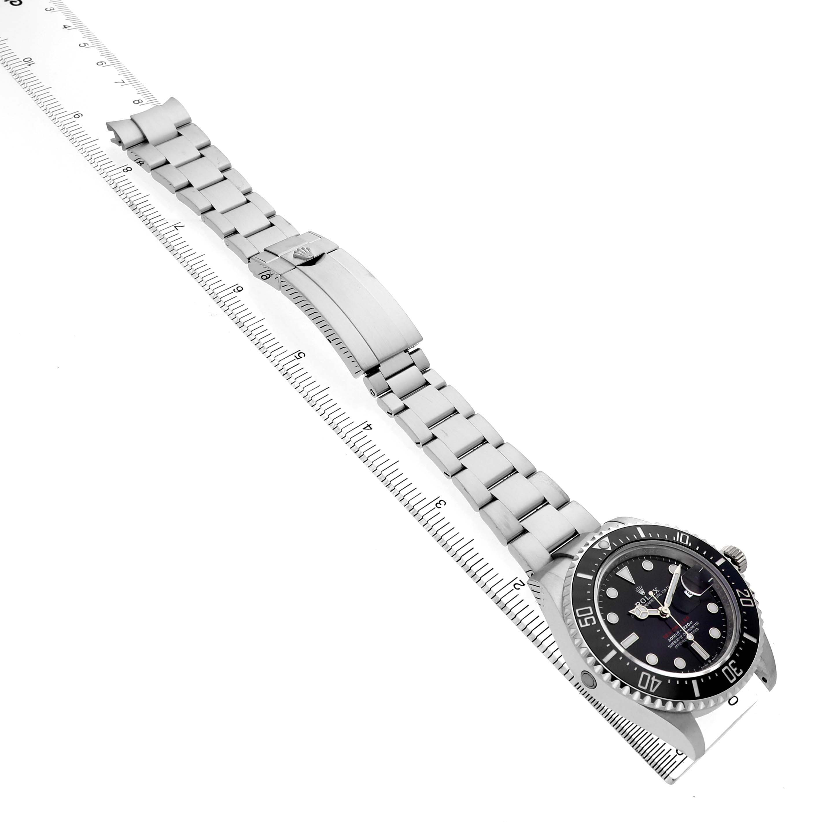 The Rolex Sea-Dweller 126600 Men's Stainless Steel Black Dial watch is shown from an overhead angle, featuring the face, bezel, and entire metal bracelet laid along a ruler.