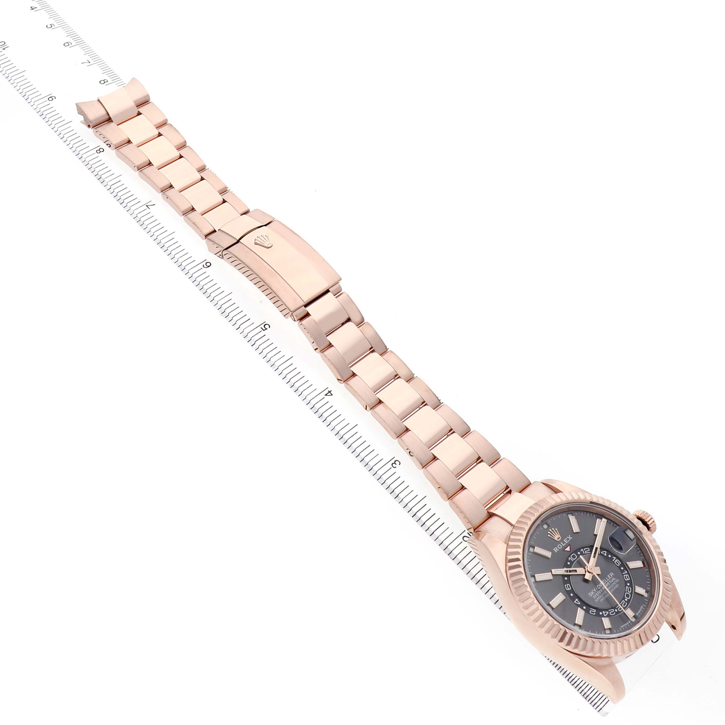 The image shows the Rolex Sky-Dweller 336935 Men's Rose Gold Grey Dial watch laid flat at an angle, highlighting the bracelet, clasp, and face next to a ruler.