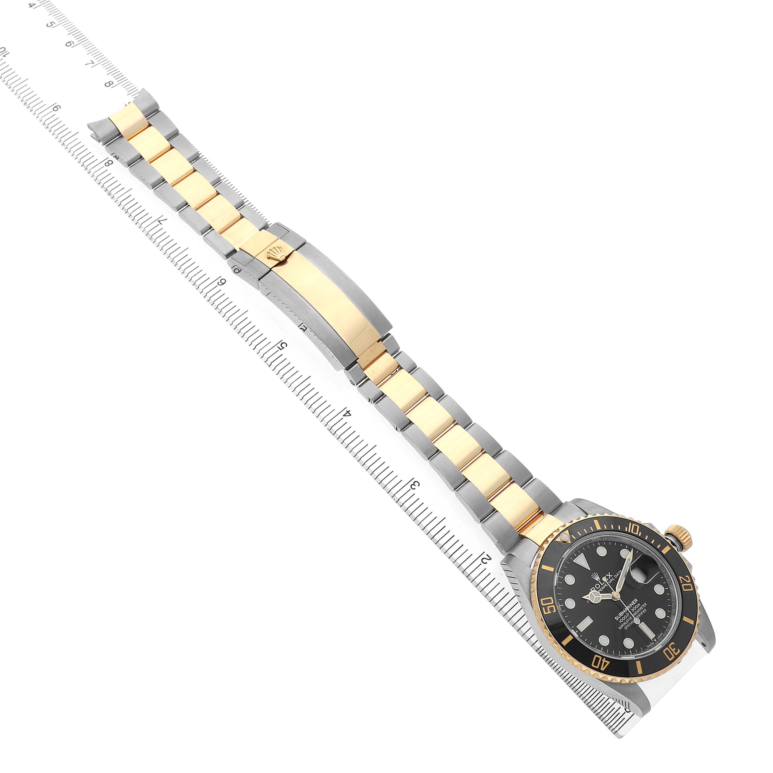 The Rolex Submariner 126613 Men's Steel and Gold (two tone) Black Dial is shown at an angled view, displaying the face and full bracelet with a ruler alongside it.