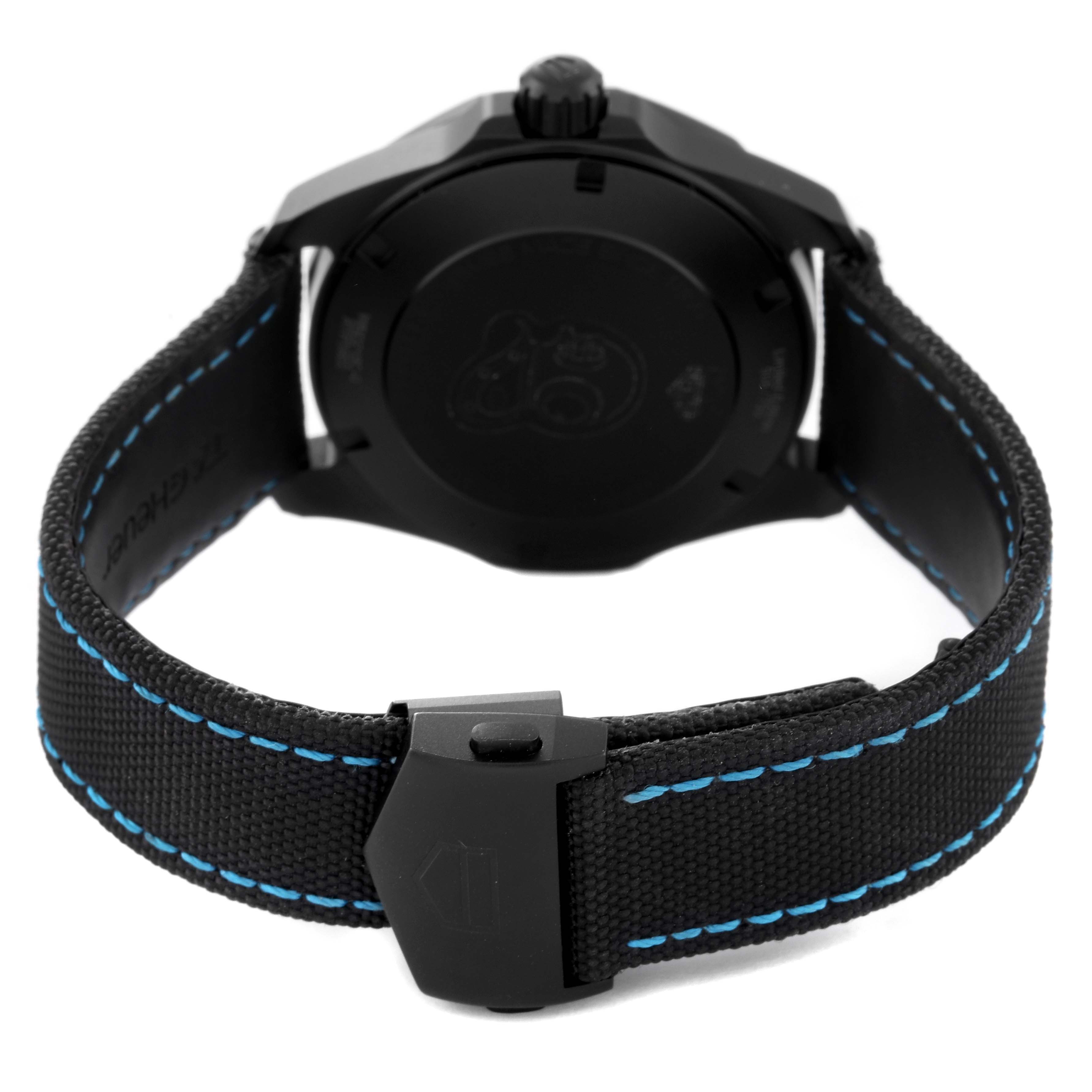 The image shows the back view of a Tag Heuer Aquaracer watch with a black case and black strap featuring blue stitching.
