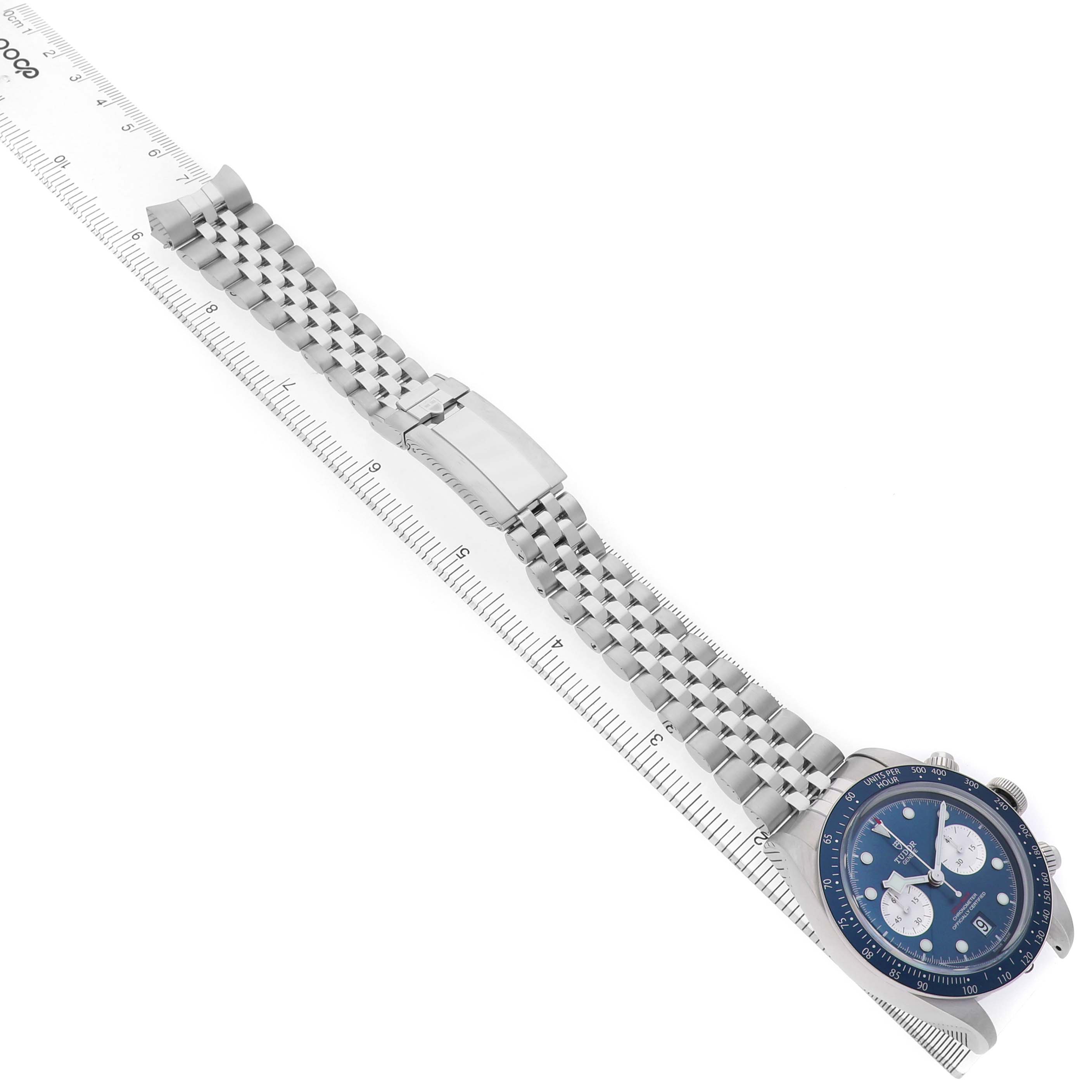 The Tudor Heritage Chrono 79360B Men's Stainless Steel Blue Dial watch is shown at a diagonal angle displaying the face, bracelet, and clasp next to a ruler.