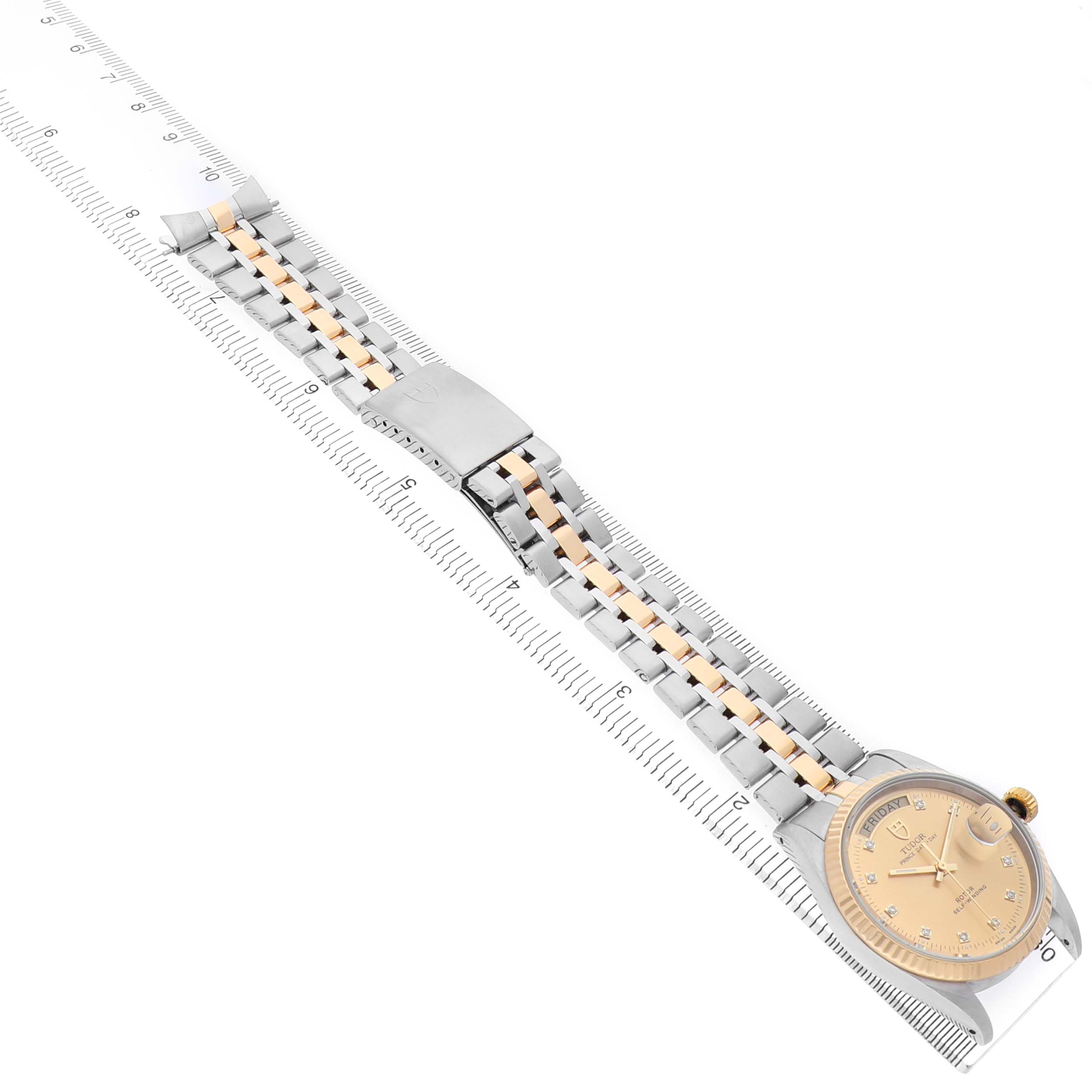The Tudor Prince 76213 Men's Stainless Steel Champagne Dial model watch is shown from a top-down angle, highlighting its face, band, clasp, and a dual-tone design on a ruler backdrop.