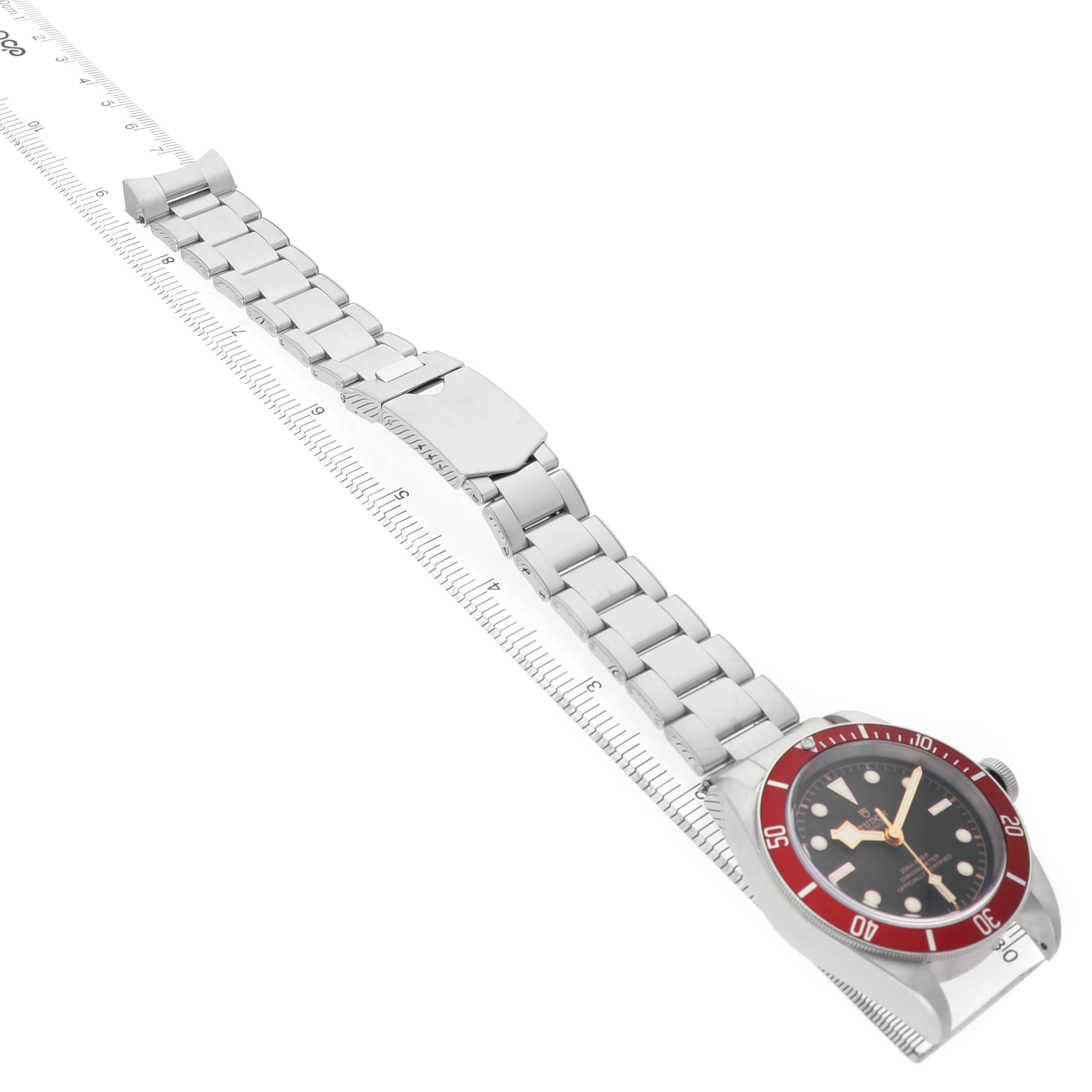 The Tudor Heritage Black Bay 79230R Men's Stainless Steel Black Dial watch is shown at a diagonal angle, highlighting the face, bezel, and full bracelet on a ruler.