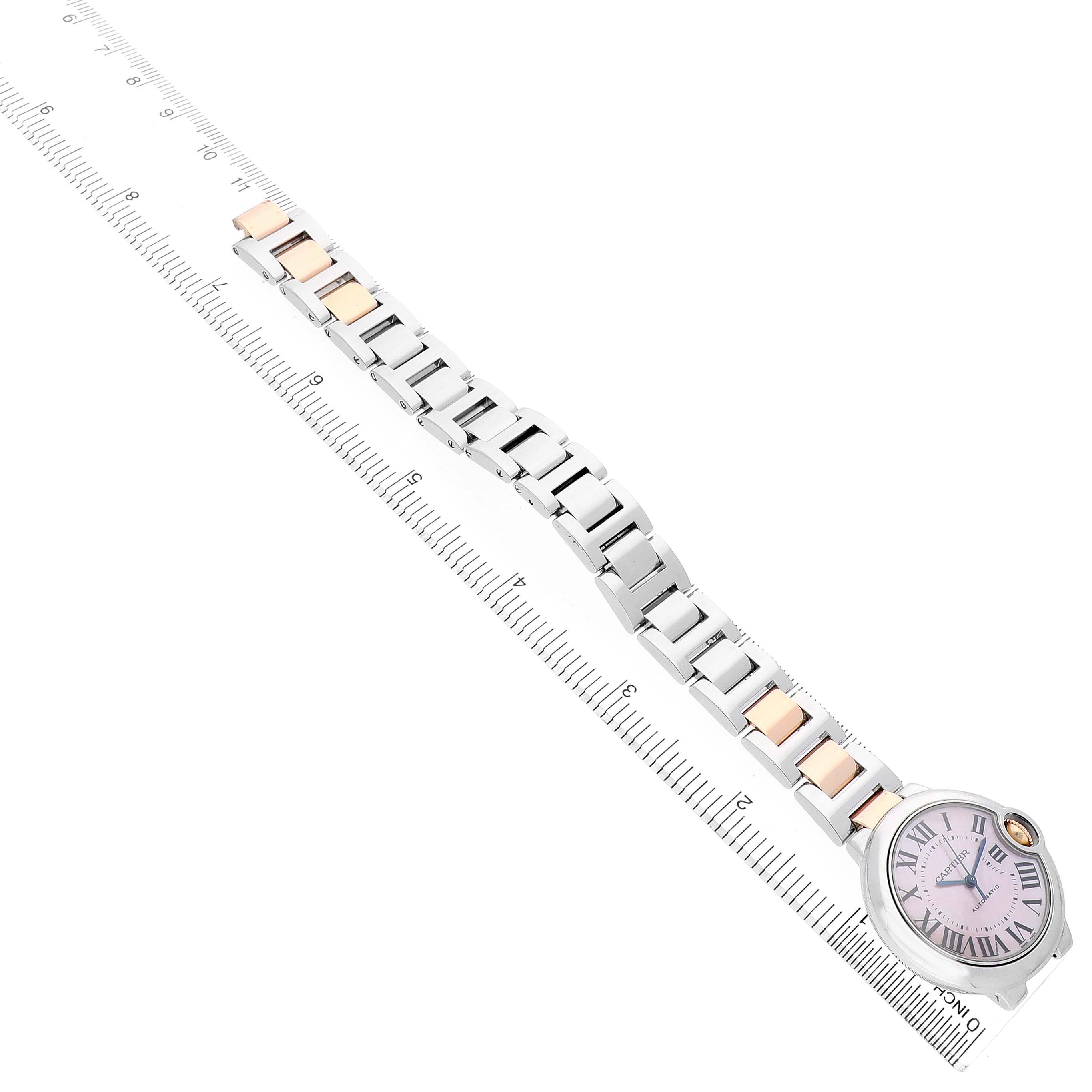 The Cartier Ballon Bleu W6920070 Women's Stainless Steel Pink Dial watch is shown from an angled top view, highlighting its bracelet and face alongside a ruler for scale.