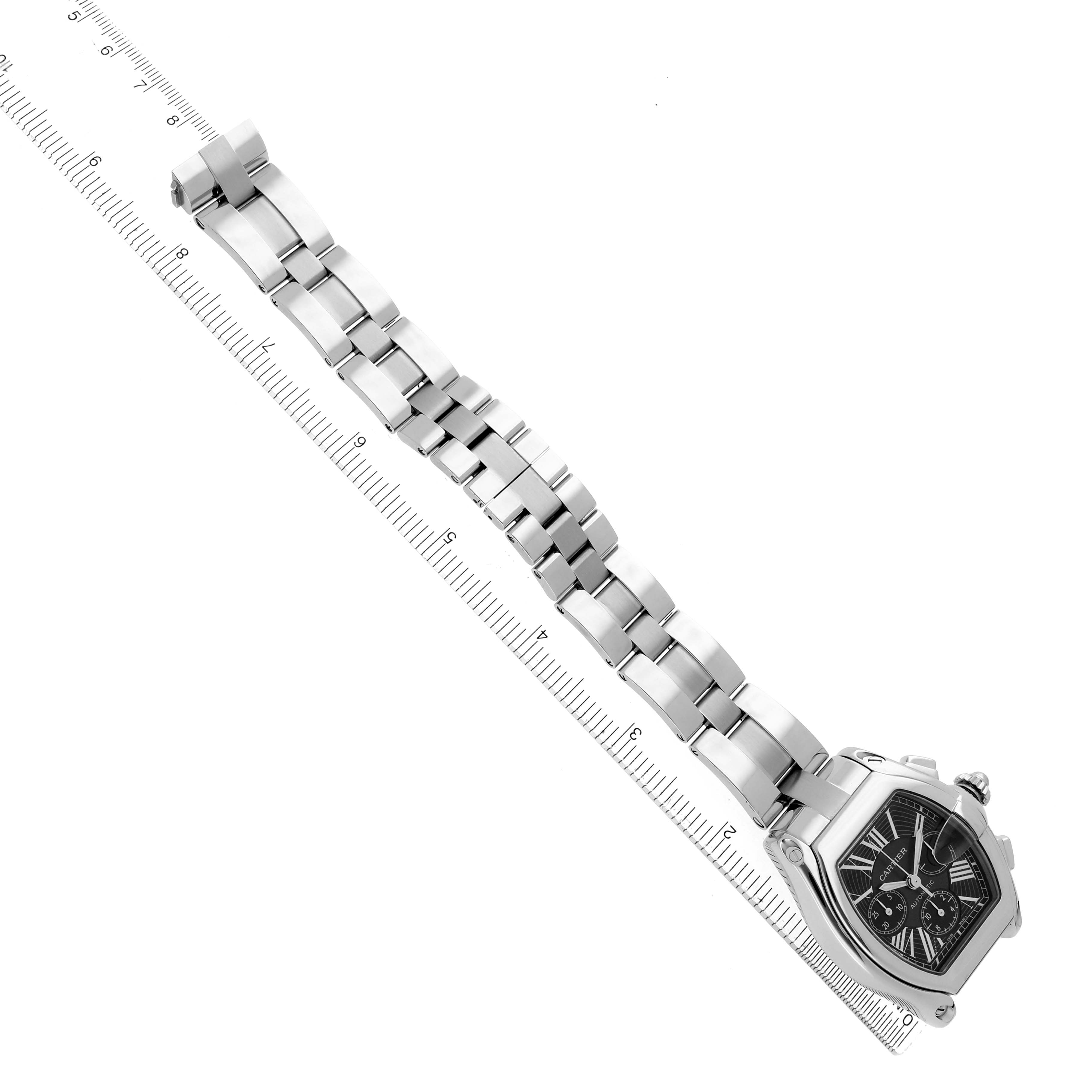 The Cartier Roadster model W62020X6 is shown from a top-down angle, displaying the full metal bracelet and watch face alongside a ruler for scale.