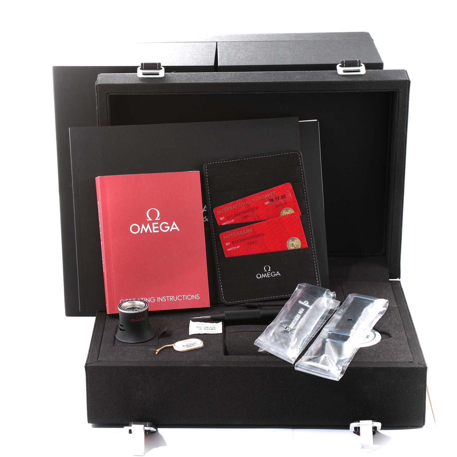 The image shows the accessories of an Omega Speedmaster 311.30.42.30.01.006 Men
s Stainless Steel Black Dial 311.30.42.30.01.006 Men
s Stainless Steel Black Dial watch, including manuals, warranty cards, a loupe, and tool kits, arranged in its box.