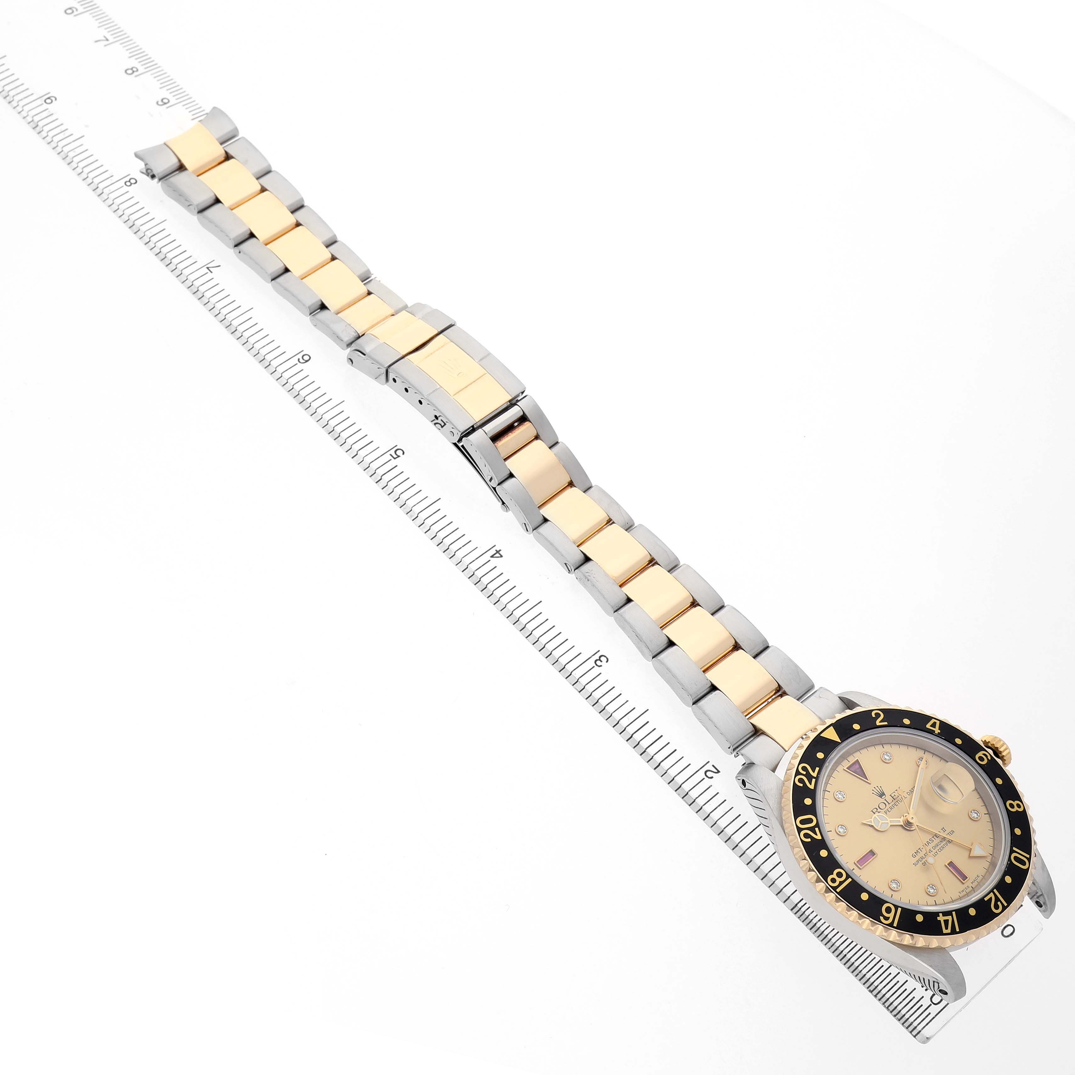 The image shows a Rolex GMT-Master 16713 Men's Stainless Steel Champagne Dial watch laid flat next to a ruler, displaying the bracelet, dial, and bezel from an overhead angle.