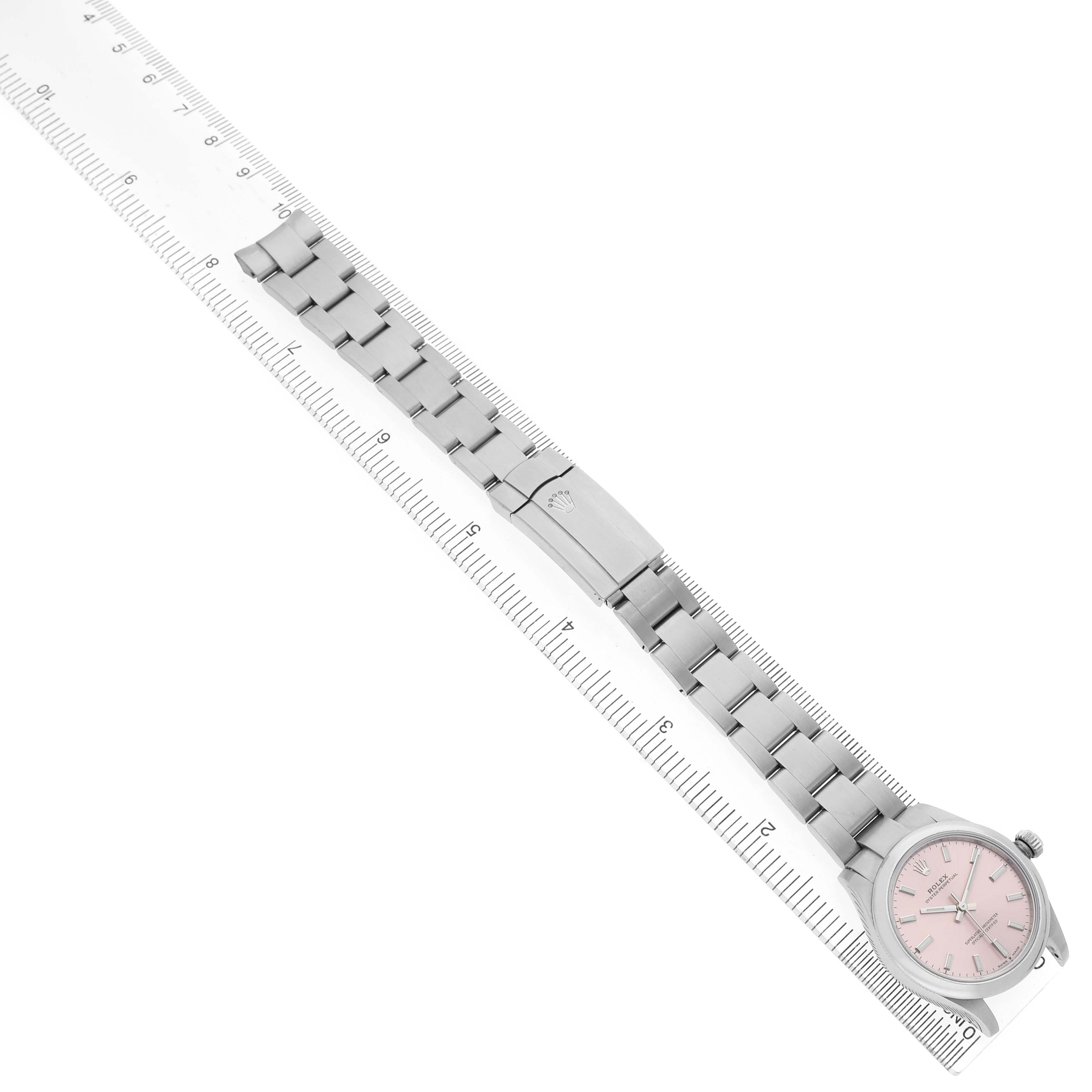 The Rolex Mid-Size 277200 Women's Stainless Steel Pink Dial watch is shown from an overhead angle, highlighting the face, bezel, and full bracelet on a ruler.