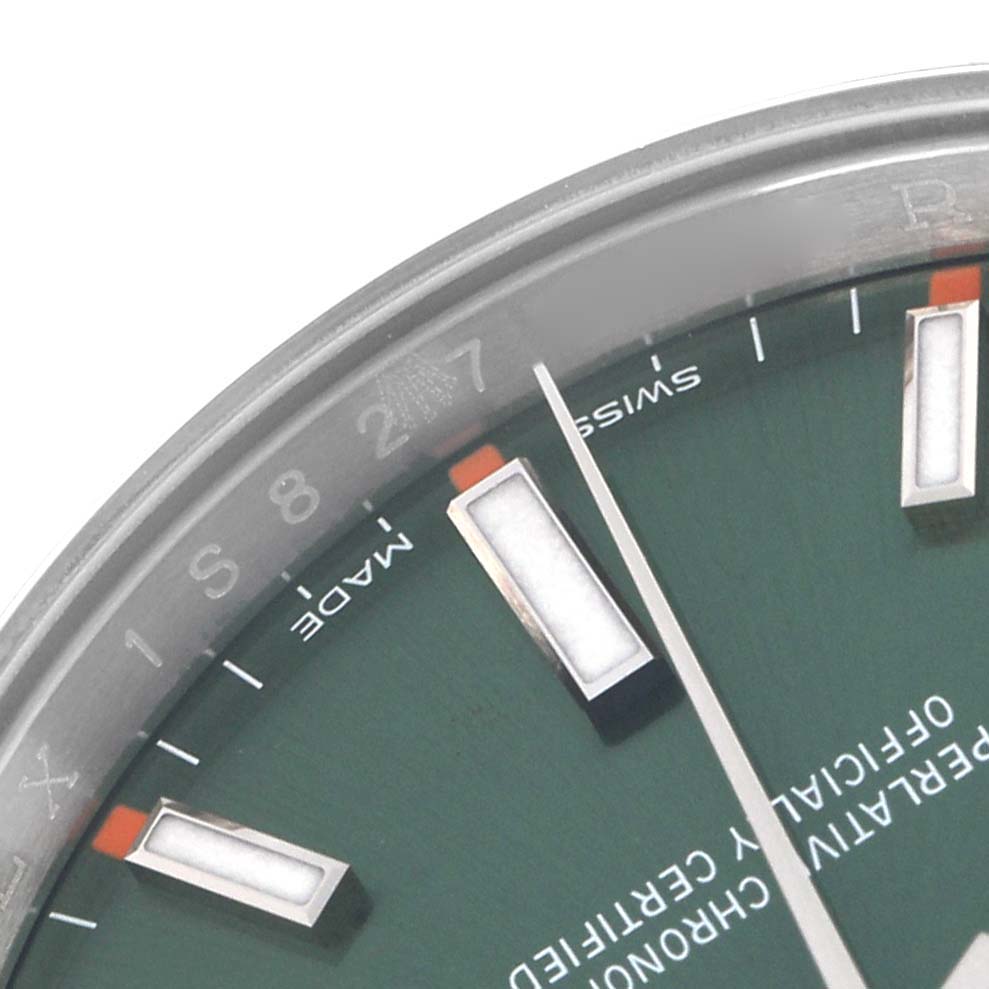 The image shows a close-up of the Rolex Oyster Perpetual model 114200 watch, highlighting the green dial, indices, and part of the bezel with "Swiss Made."
